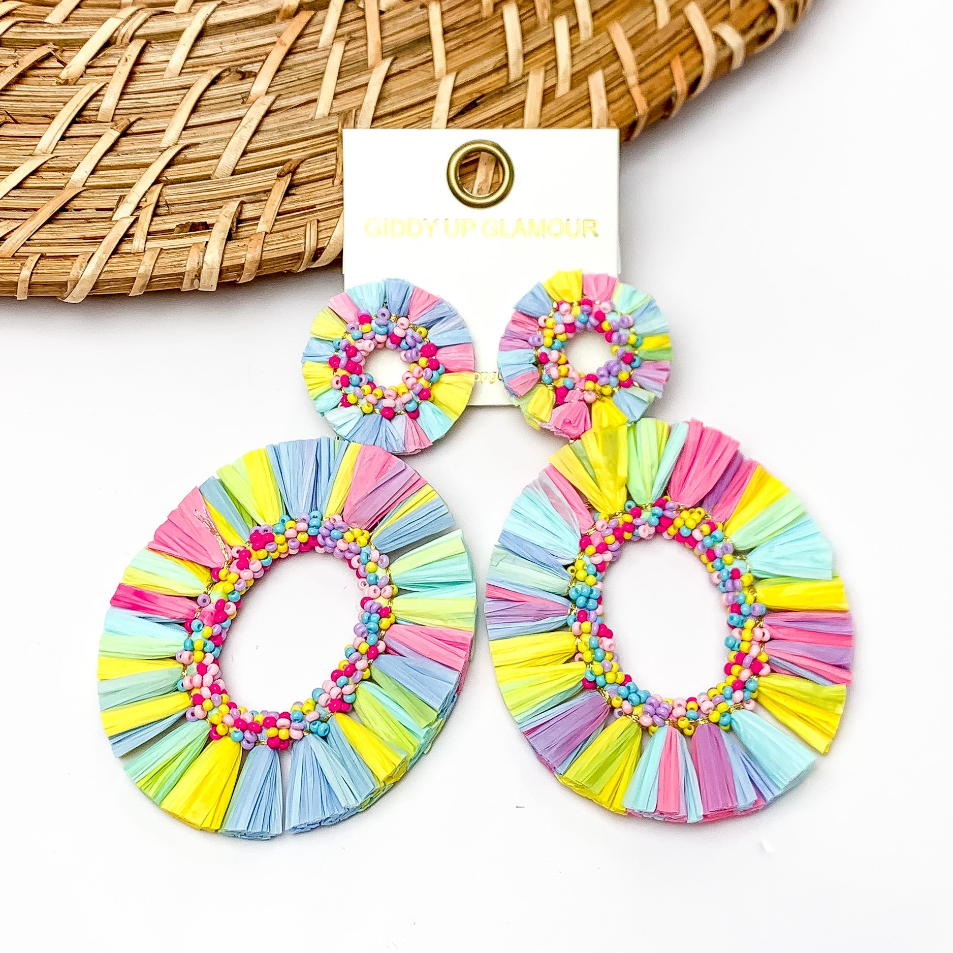Siesta Keys Raffia Wrapped Open Oval Earrings in Multicolor. Pictured on a white background with a wood like piece in the top left.