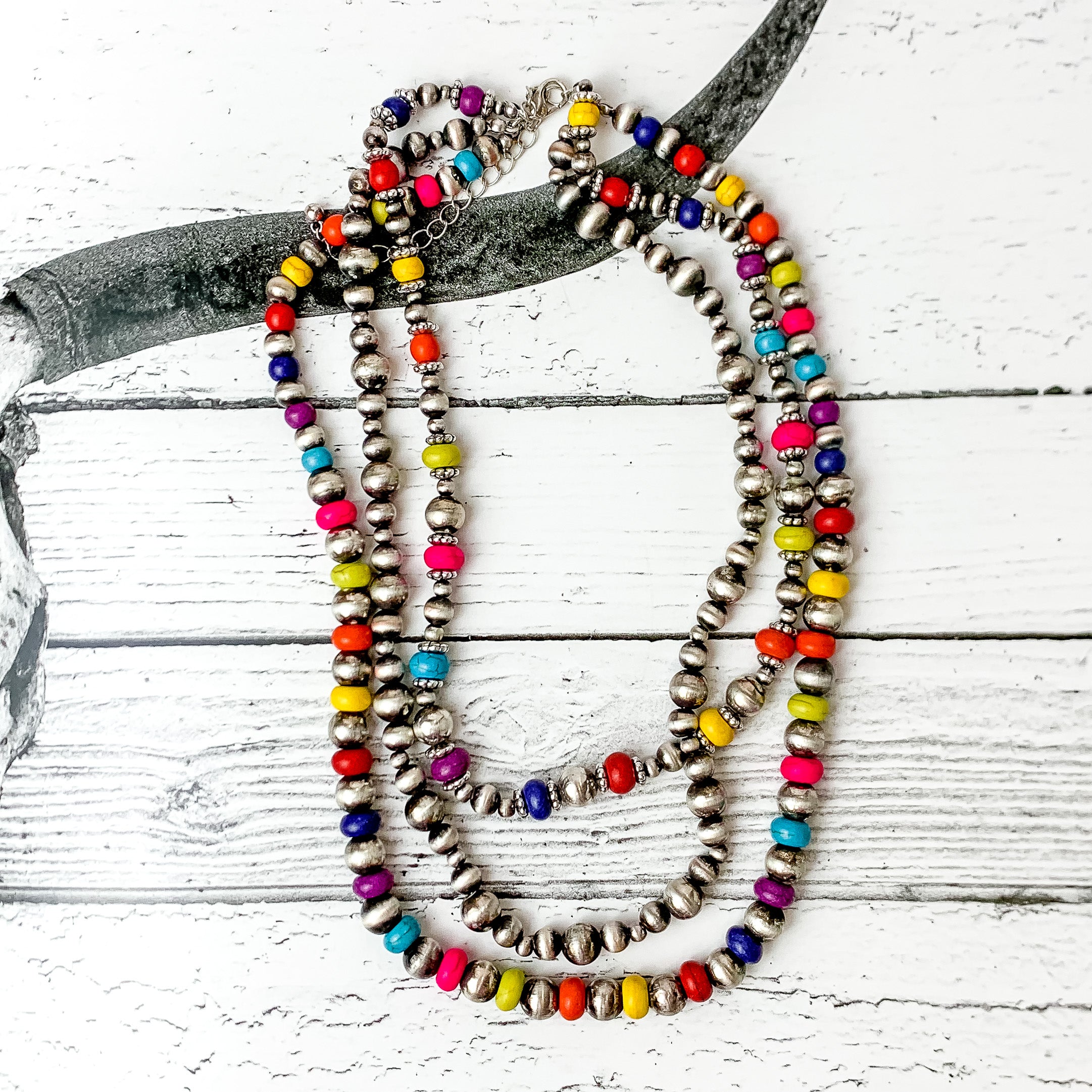 This necklace comes with three strands of beads. Two of them are mixed with multi colored beads and faux navajo pearls in silver. The other strand is just faux navajo pearls in silver. Pictured on a black and white western photo in the background.