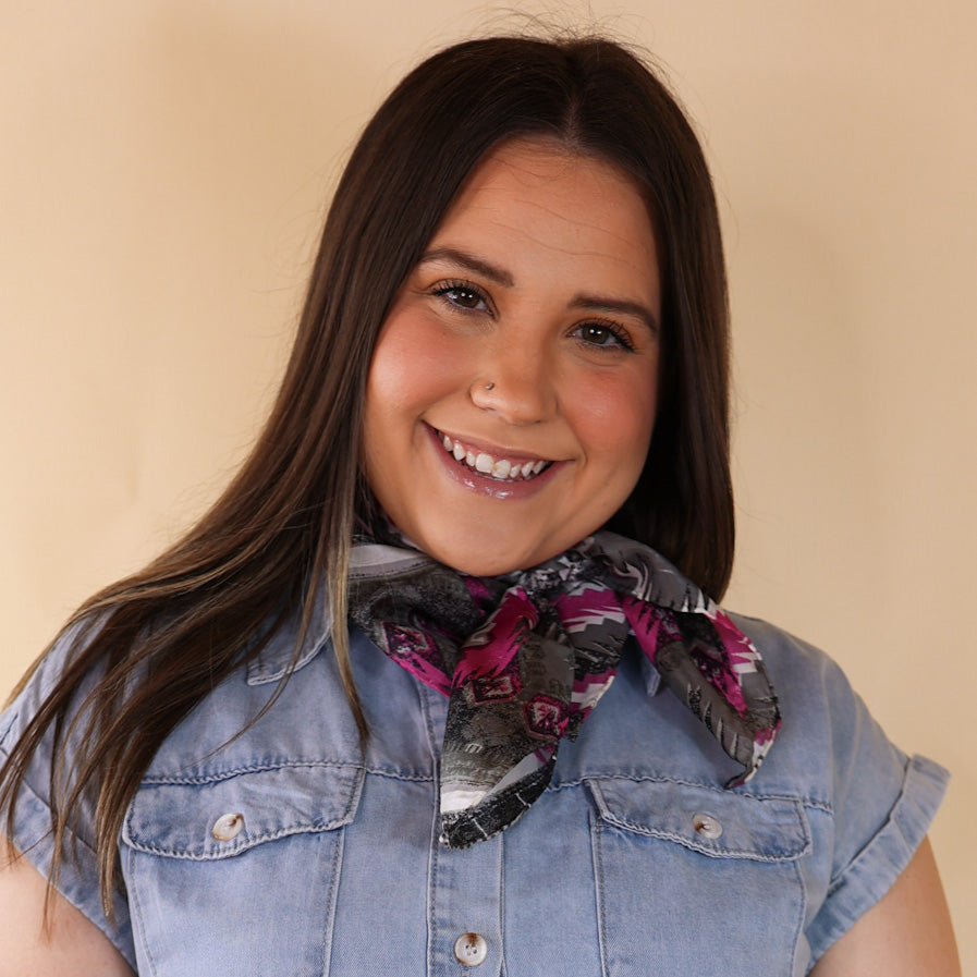 Brunette model is pictured wearing a denim button up top and a silver and pink aztec printed printed scarf tied around her neck. She is pictured in front of a beige background. 
