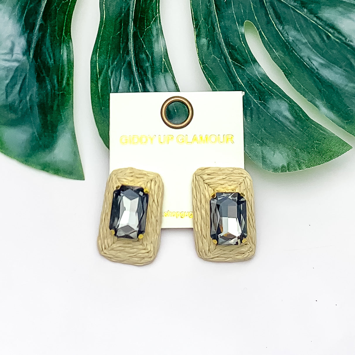 Truly Tropical Raffia Rectangle Earrings in Ivory With Grey Crystal. Pictured on a white background with the earrings laying on a large leaf.