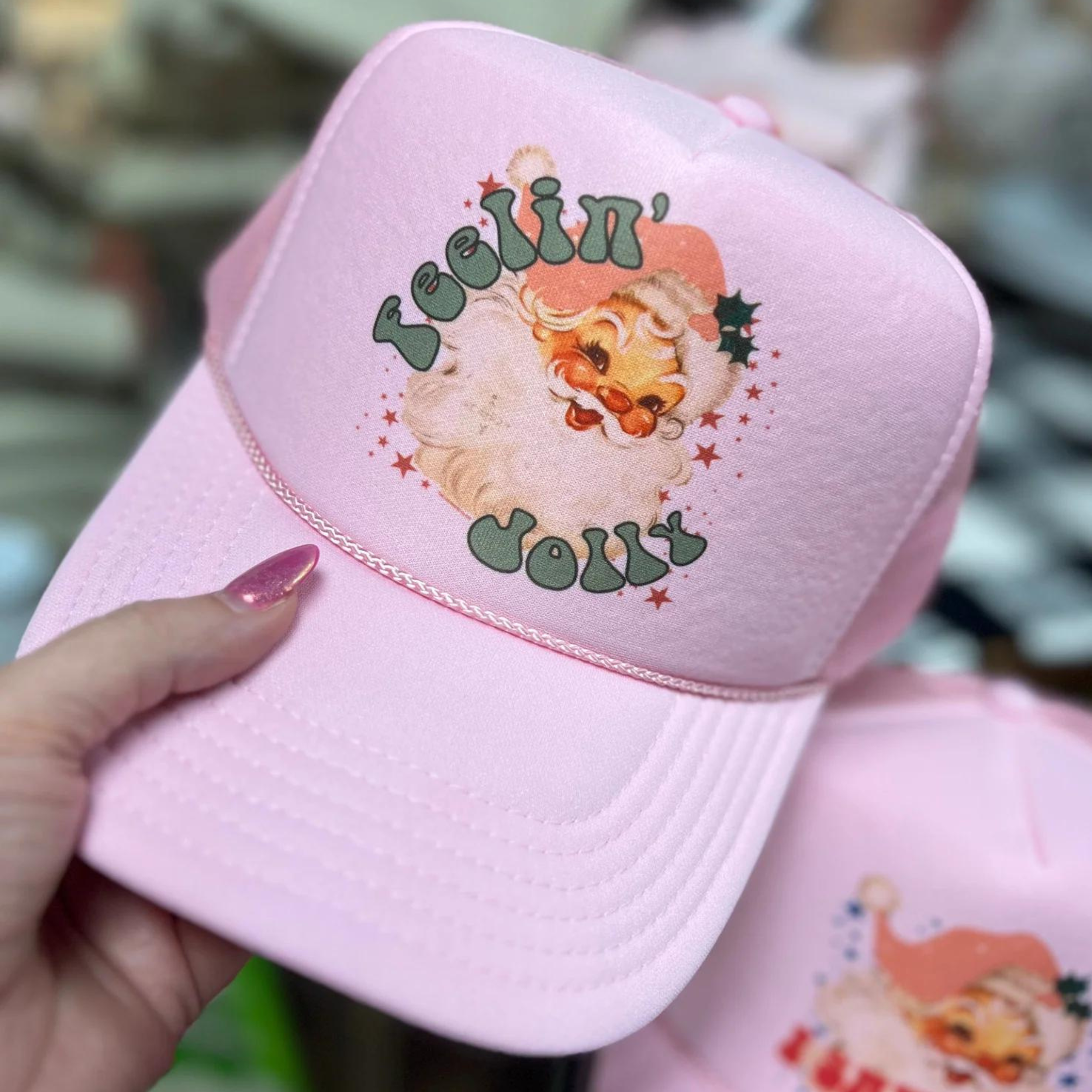 Photo features a light pink trucker hat with the saying "Feelin' Jolly" and a picture of Santa on the front.