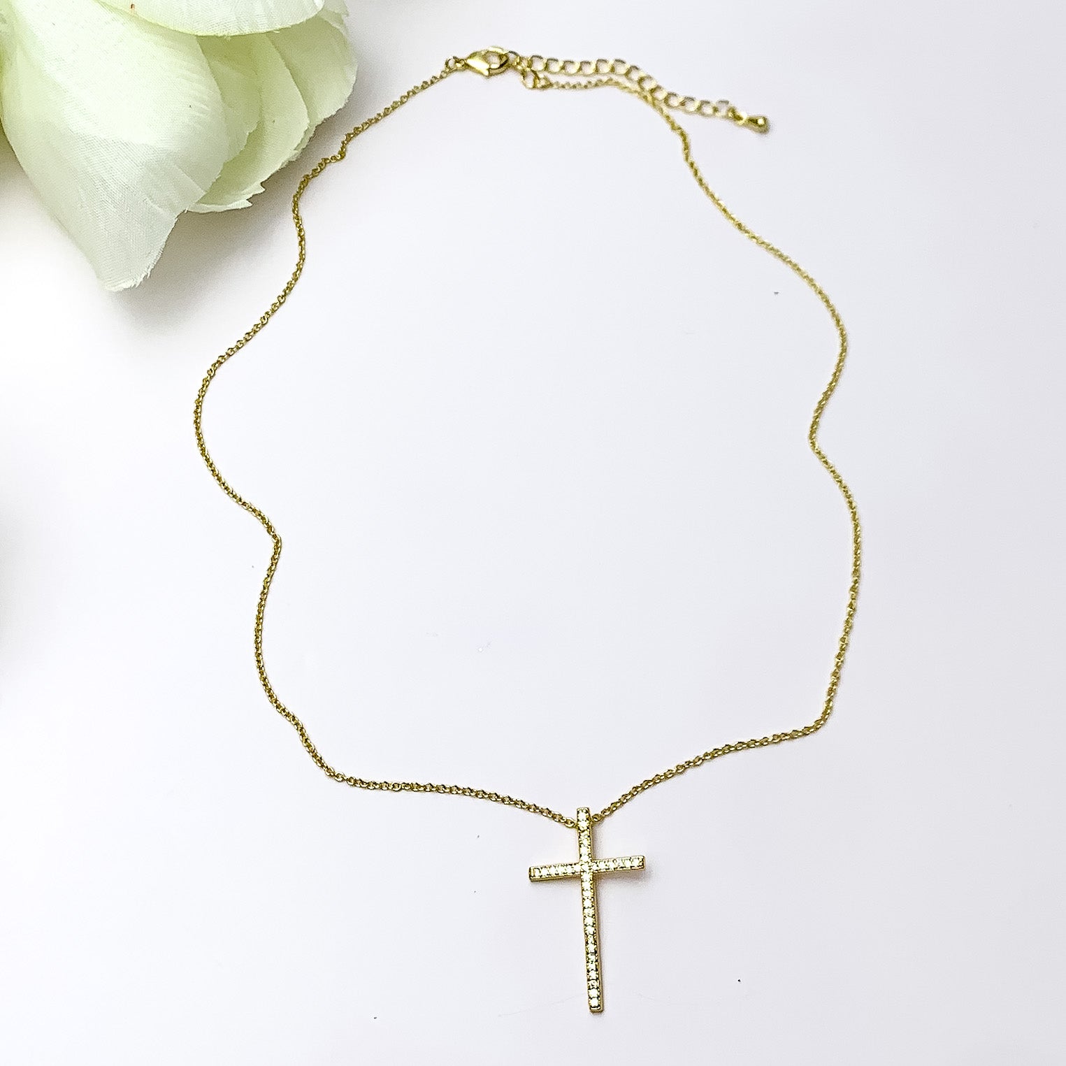 Gold Tone Necklace With Clear Crystal Cross Charm. Pictured on a white background with a piece of wood behind the necklace.