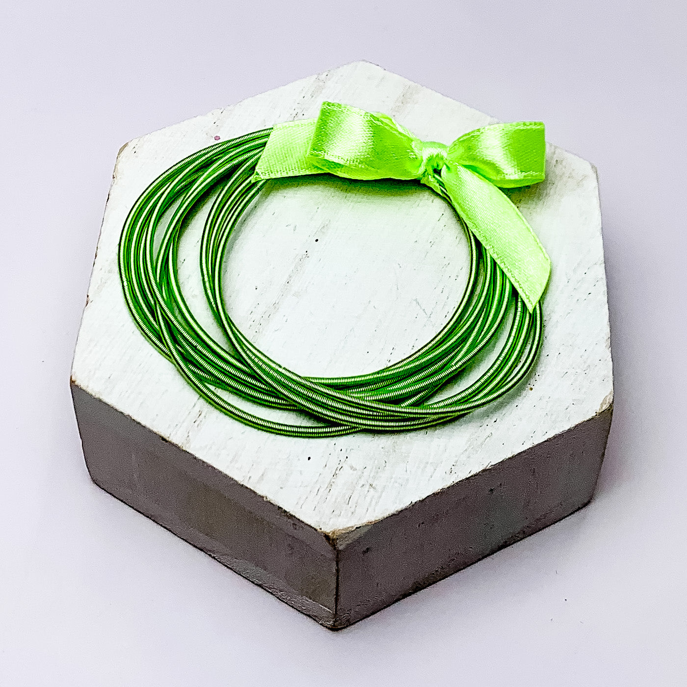 Guitar String Bracelets with Bow in Light Green. Pictured o n a white background sitting on top of a white block.