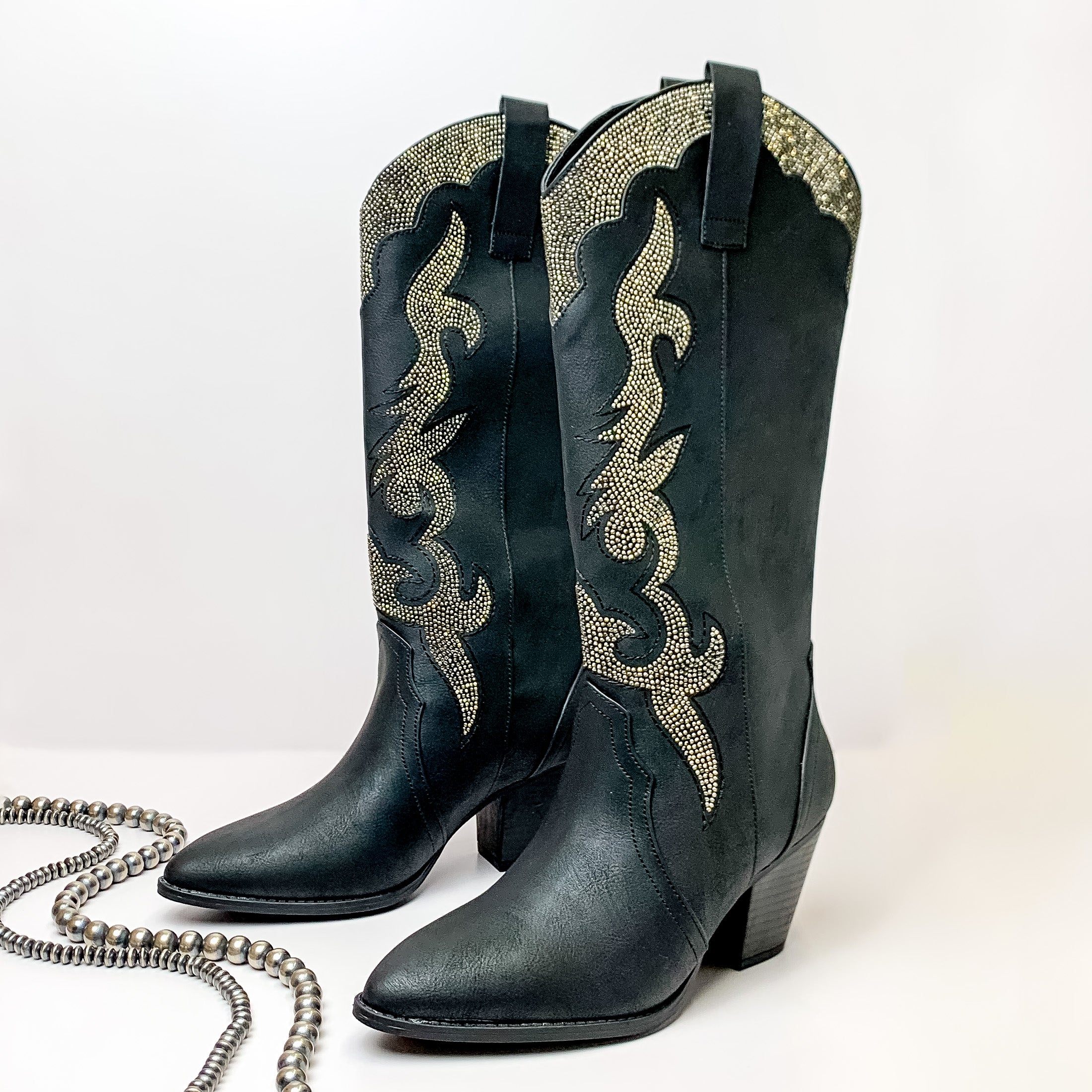 Pictured is a pair of black, western boots with a black heel. These boots have a charcoal crystal design. These boots are pictured on a white background with silver beads in front of the boots. 