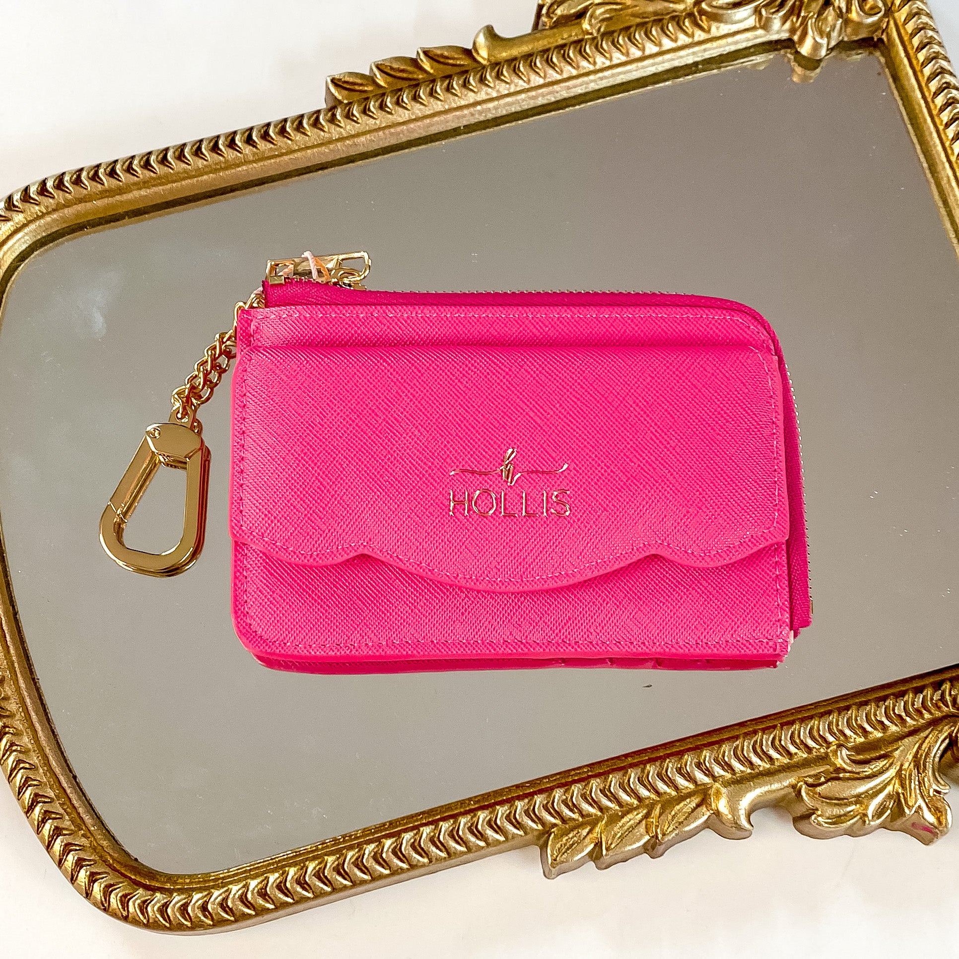 Hollis brand card holder wallet in hot pink. Wallet also has a gold chain connected to it. Pictured on a mirror with a gold frame.