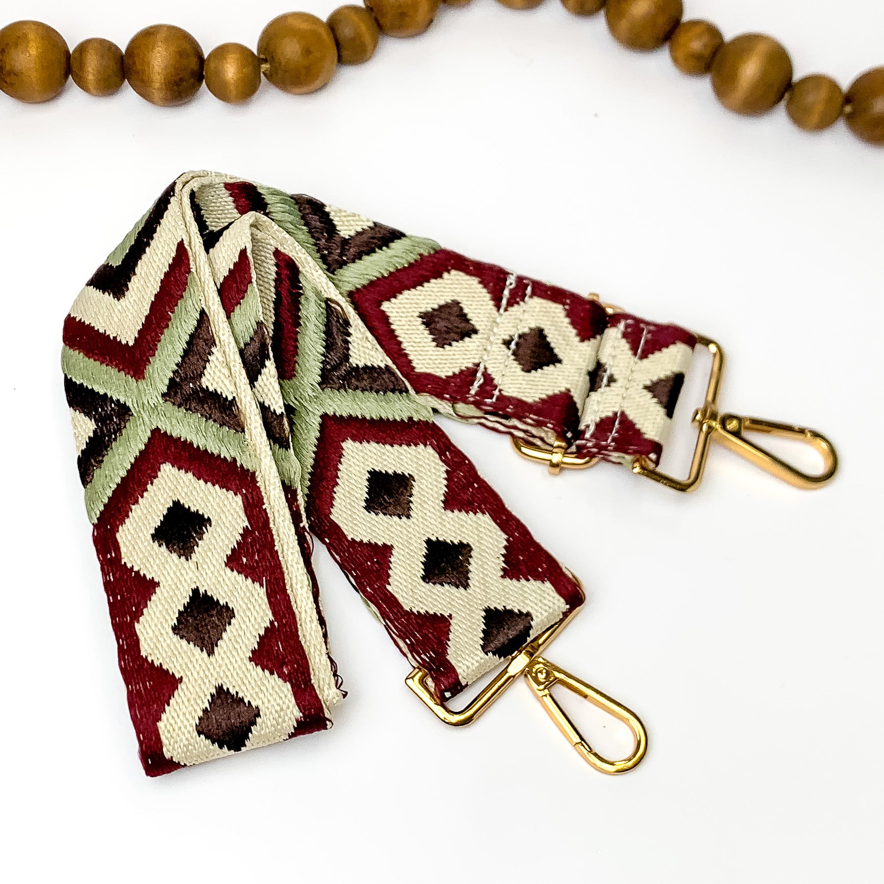 Beige canvas purse strap with dark brown, maroon, and olive green embroidered design. This purse strap includes gold accents. This purse strap is pictured on a white background with wood beads at the top.