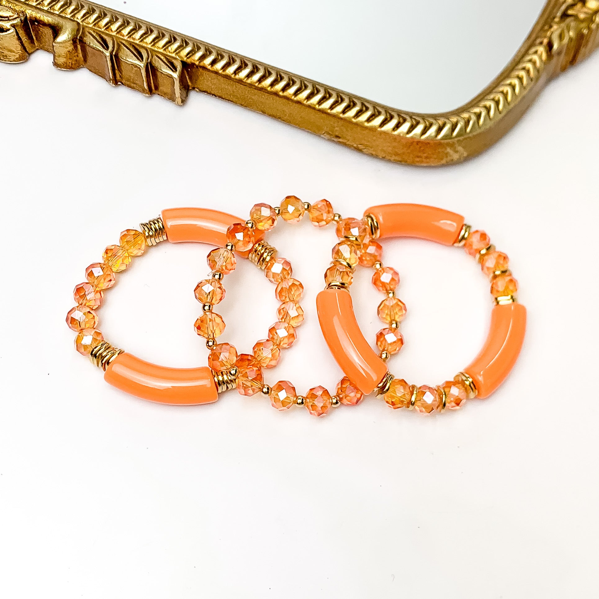 Set of Three | Sunny Bliss Crystal Beaded Bracelet Set in Orange. Pictured on a white background with a gold trimmed mirror above the bracelets.