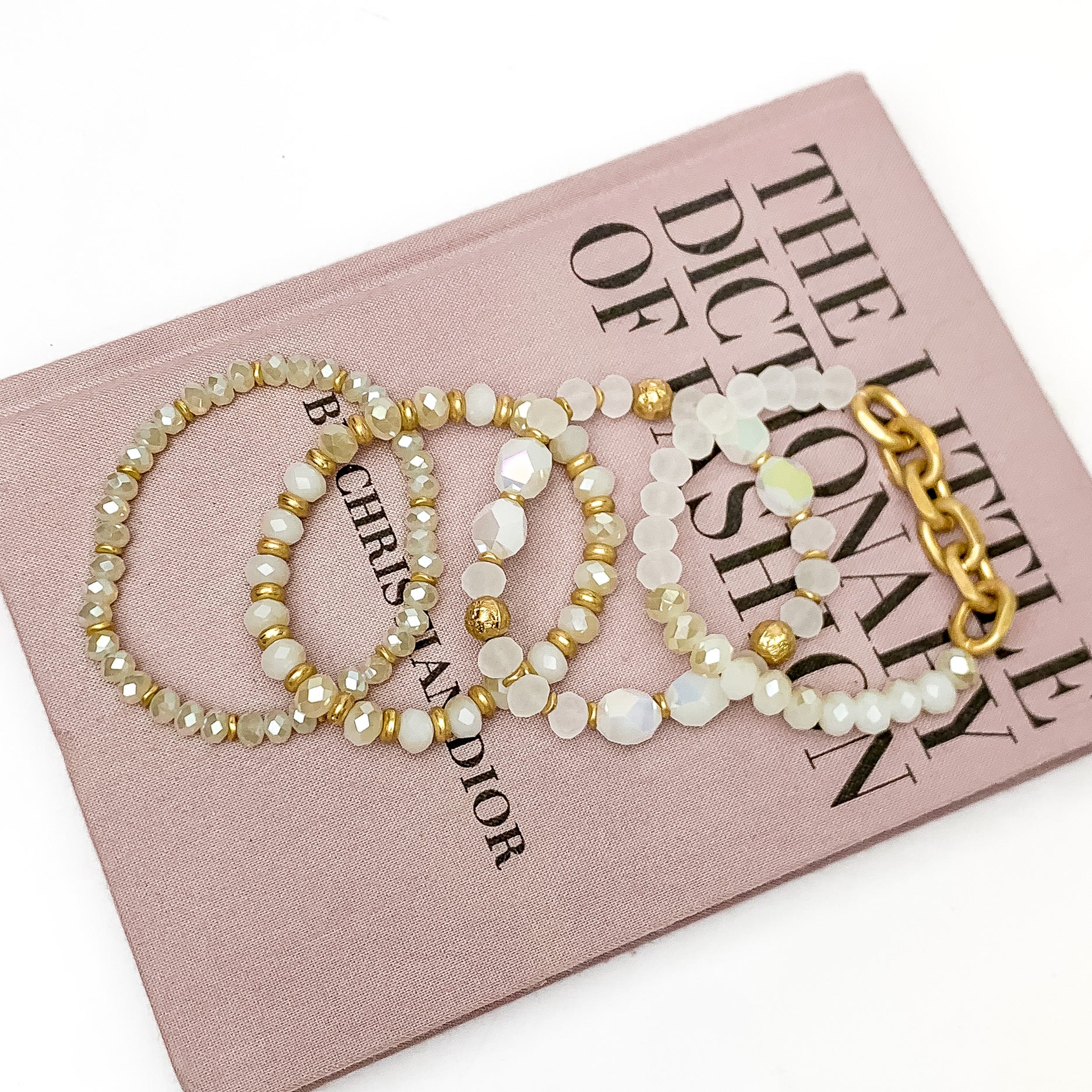 Set of Four | Glorious Gold Crystal Beaded Bracelet Set in White. Pictured laying on a closed book. The book is on a white background.