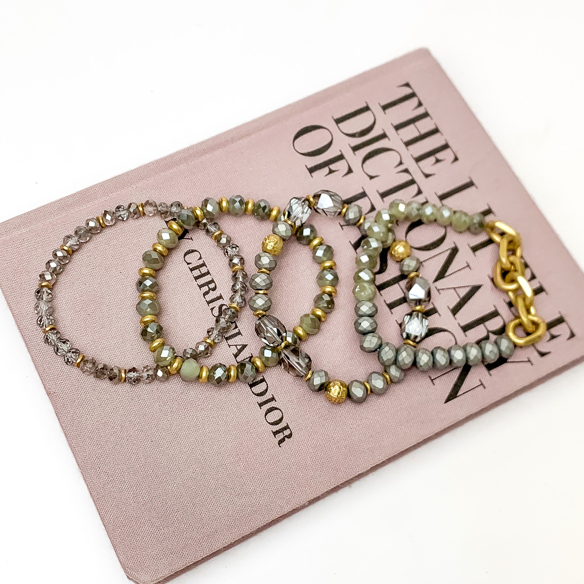 Set of Four | Glorious Gold Crystal Beaded Bracelet Set in Grey. Pictured laying on a closed book. The book is on a white background.