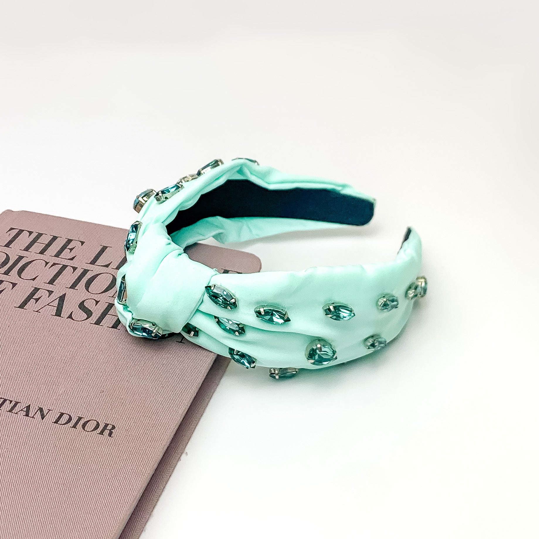 Crystal Detailed Knot Headband in Mint Green. Pictured on a white background with the headband laying against a pink book. 