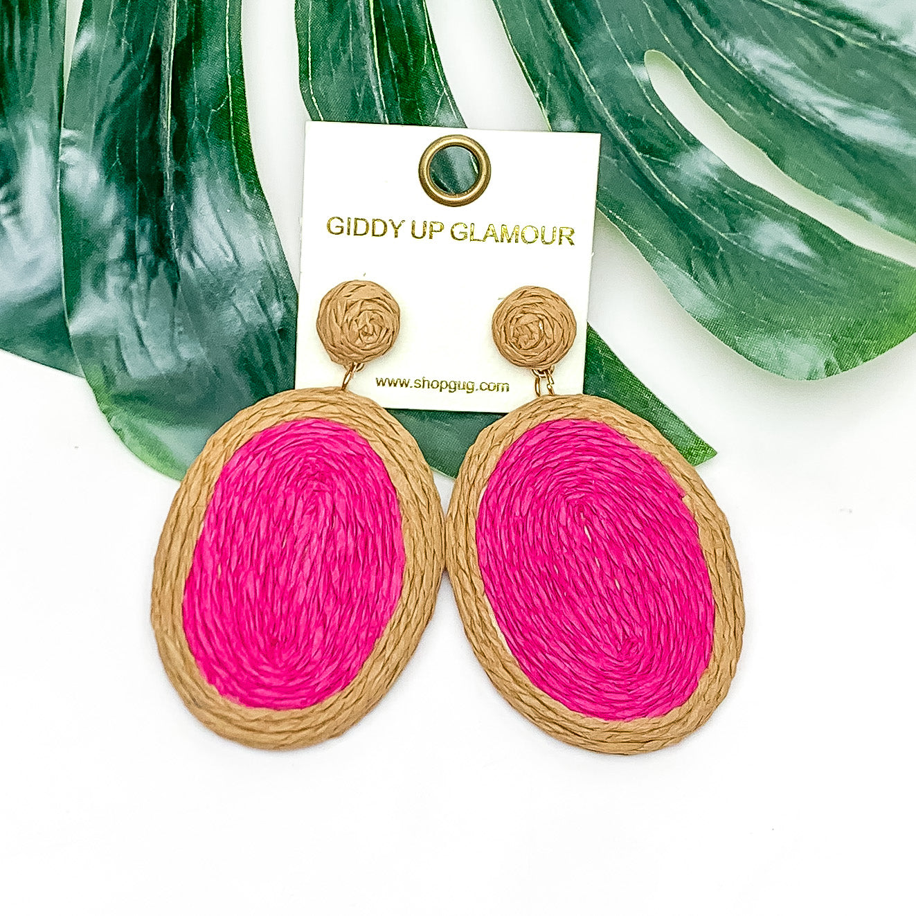 Brunch Bash Raffia Wrapped Oval Earrings in Hot Pink. Pictured on a white background with a large leaf behind the earrings.