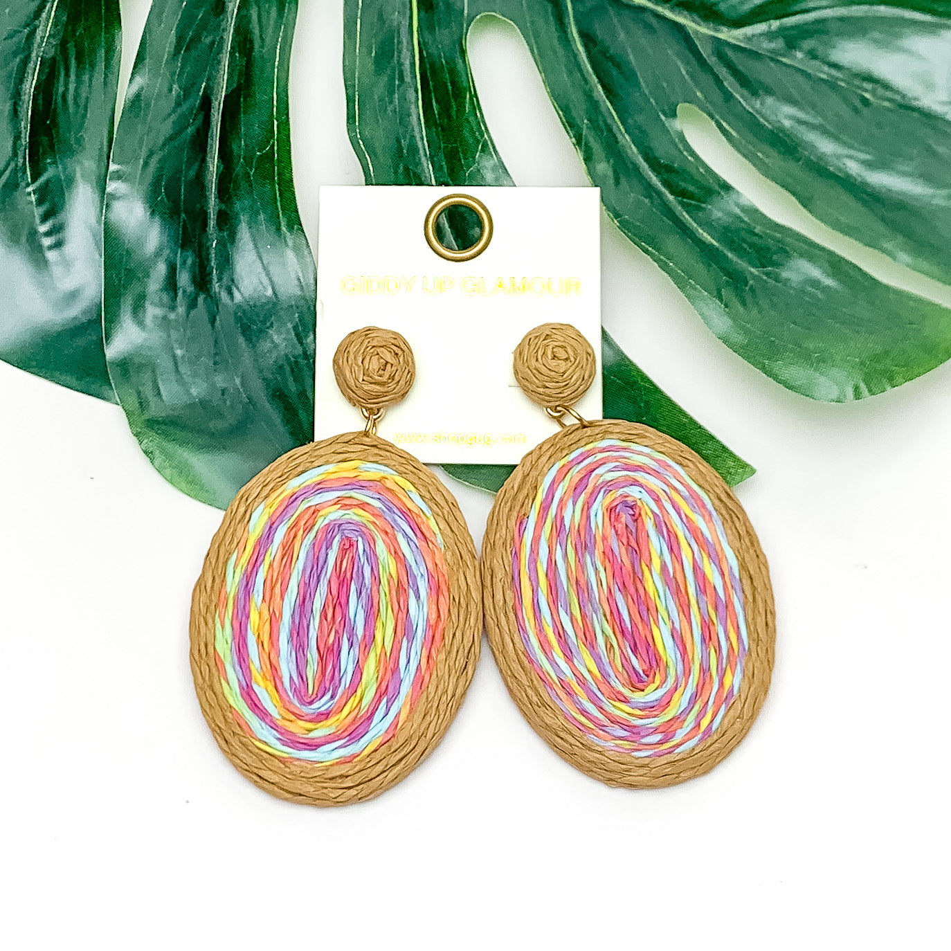 Brunch Bash Raffia Wrapped Oval Earrings in Multicolor. Pictured on a white background with a large leaf behind the earrings.