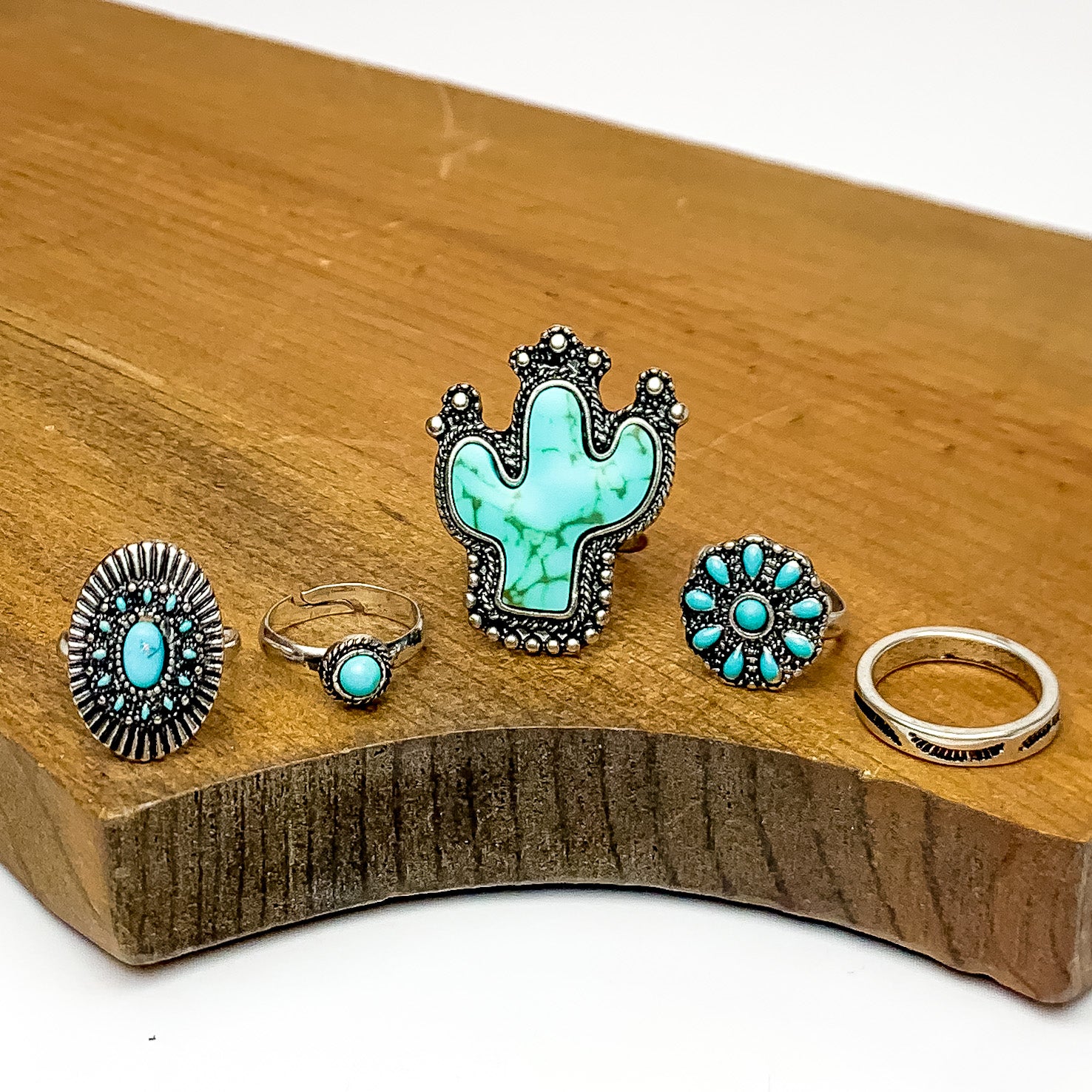 Set of 5 | Western Silver Tone Ring Set With Turquoise Stones. Pictured on a white background with the rings on a piece of wood.