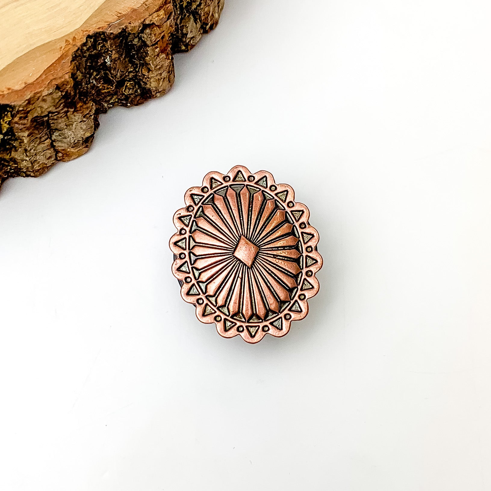 Copper tone oval phone grip. Pictured on a white background with a wood piece in the top left corner.