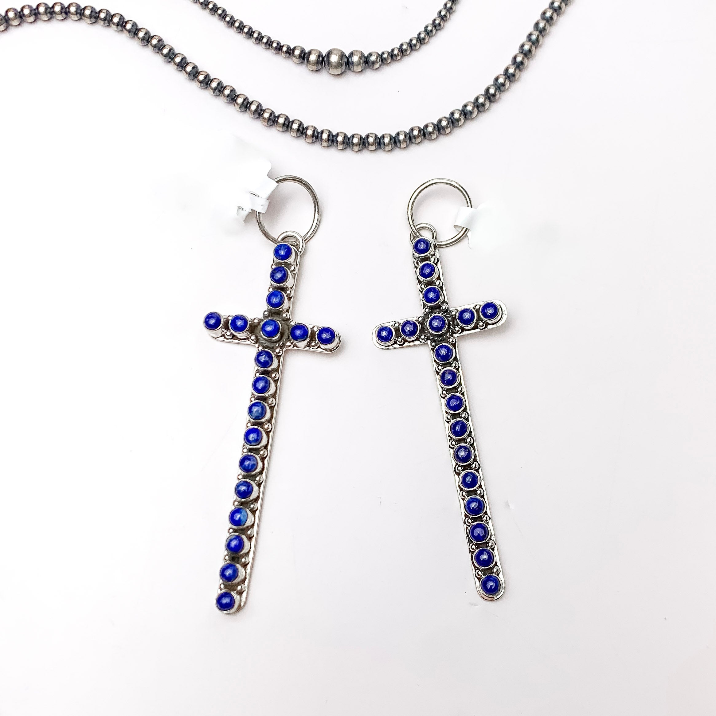 Centered in the picture is a large cross pendant with dark lapis stones. Navajo pearls are laid to the top of the pendant. All on a white background.