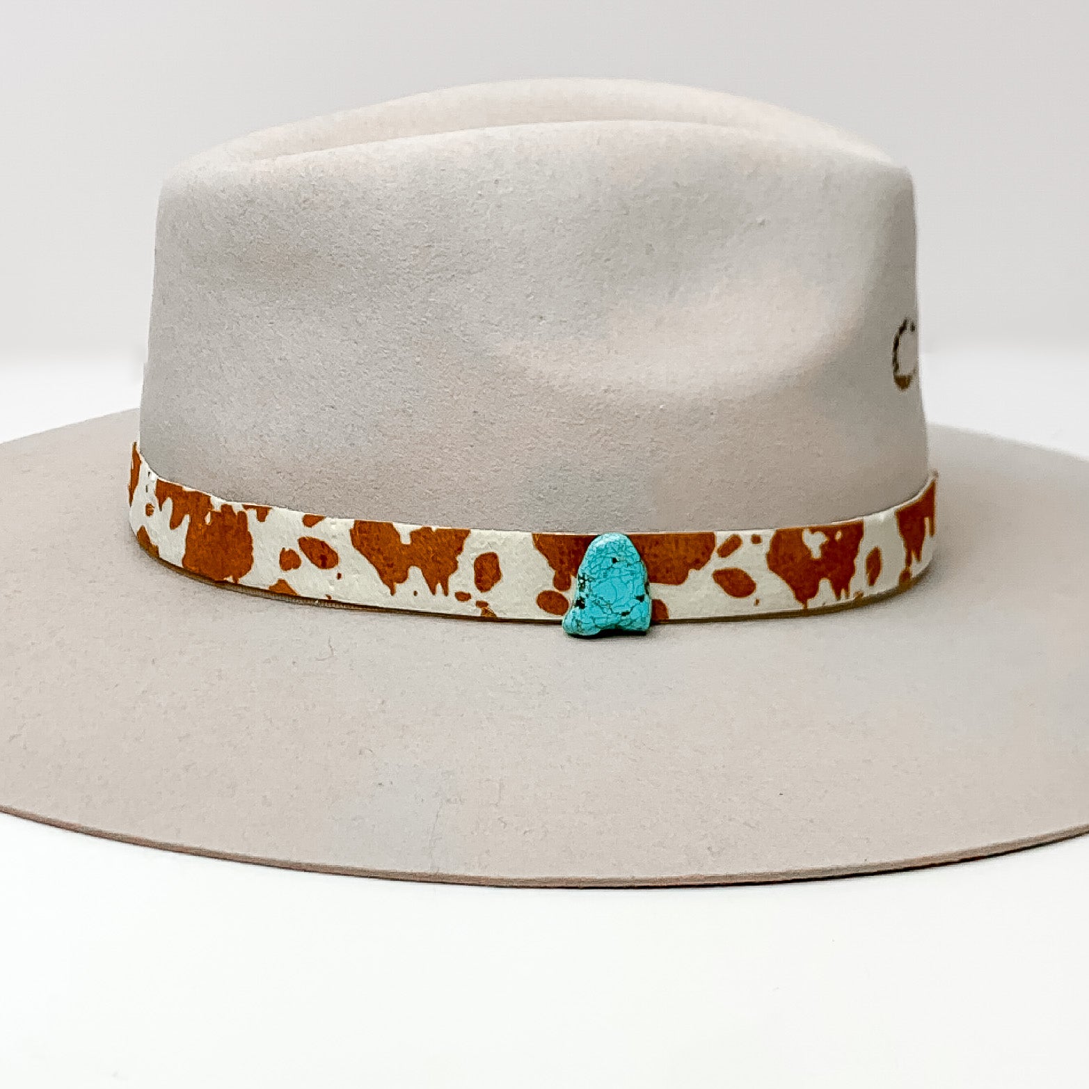 Cow Print Hat Band with Faux Turquoise Charm in Brown, and Ivory. Pictured on a white background with the band around a light tan/ brown hat.
