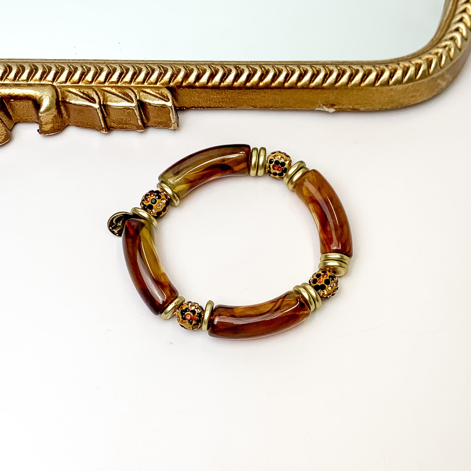 Pictured is one bracelet that has a tortoise print bamboo beads, gold beads, and crystal beads. This bracelet is pictured in front of a gold mirror on a white background. 