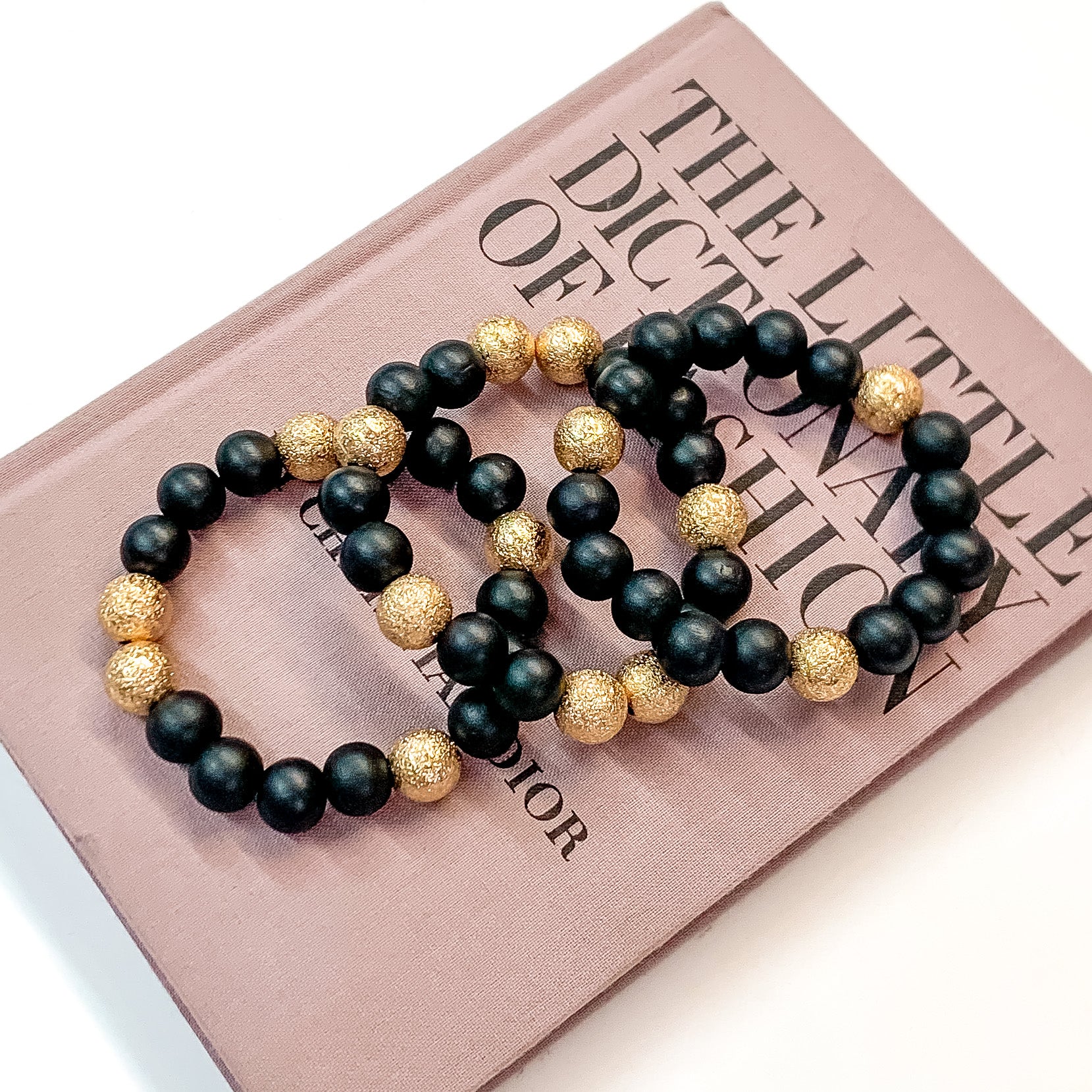 Pictured on a mauve colored book is a set of black beaded bracelets with gold beaded spacers. 