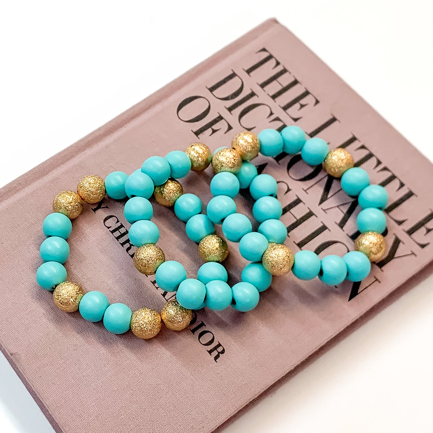 Pictured on a mauve colored book is a set of sky blue beaded bracelets with gold beaded spacers. 