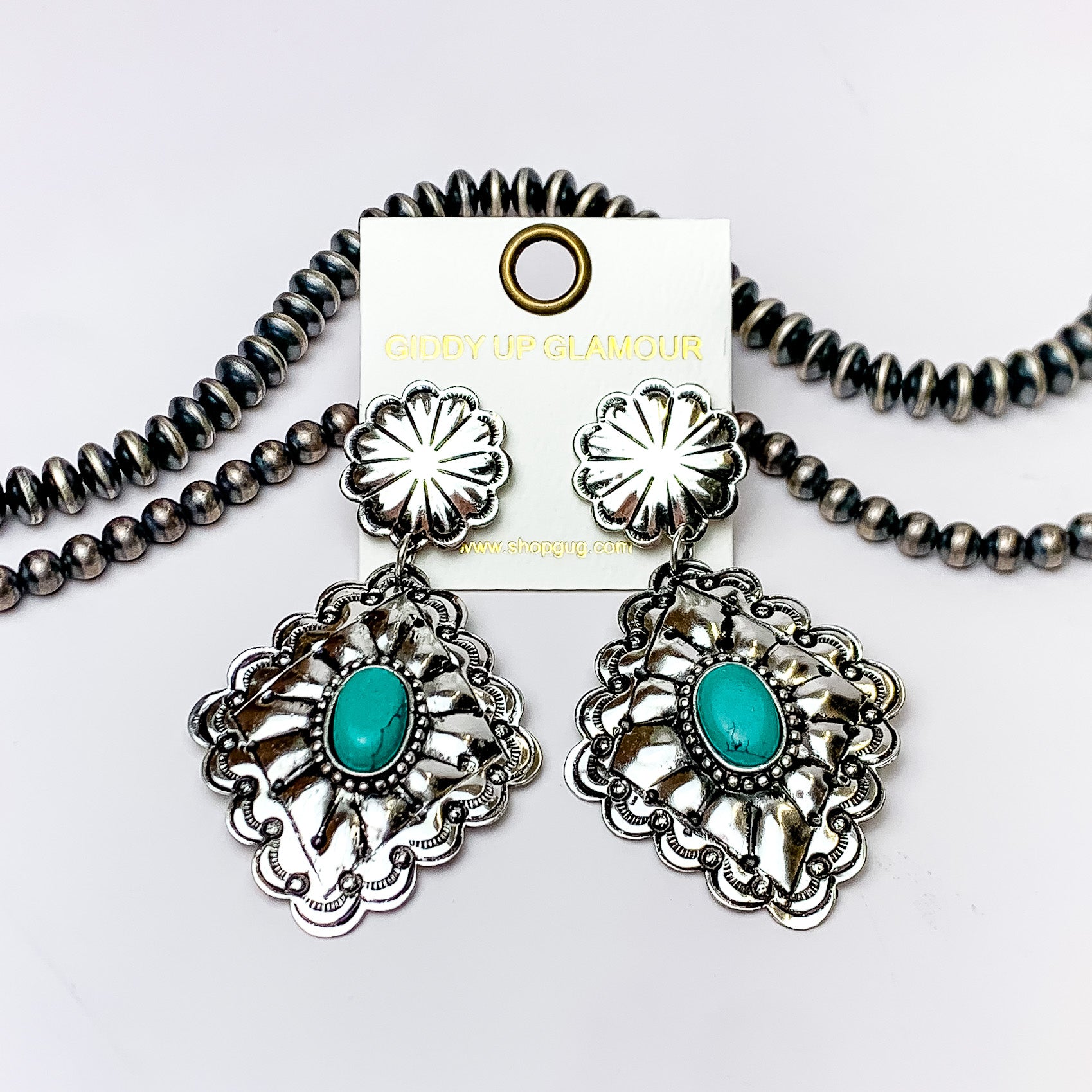 Silver circle post back earrings with a diamond concho drop and center turquoise stone. These earrings are pictured on a white background with silver beads at the top of the picture. 