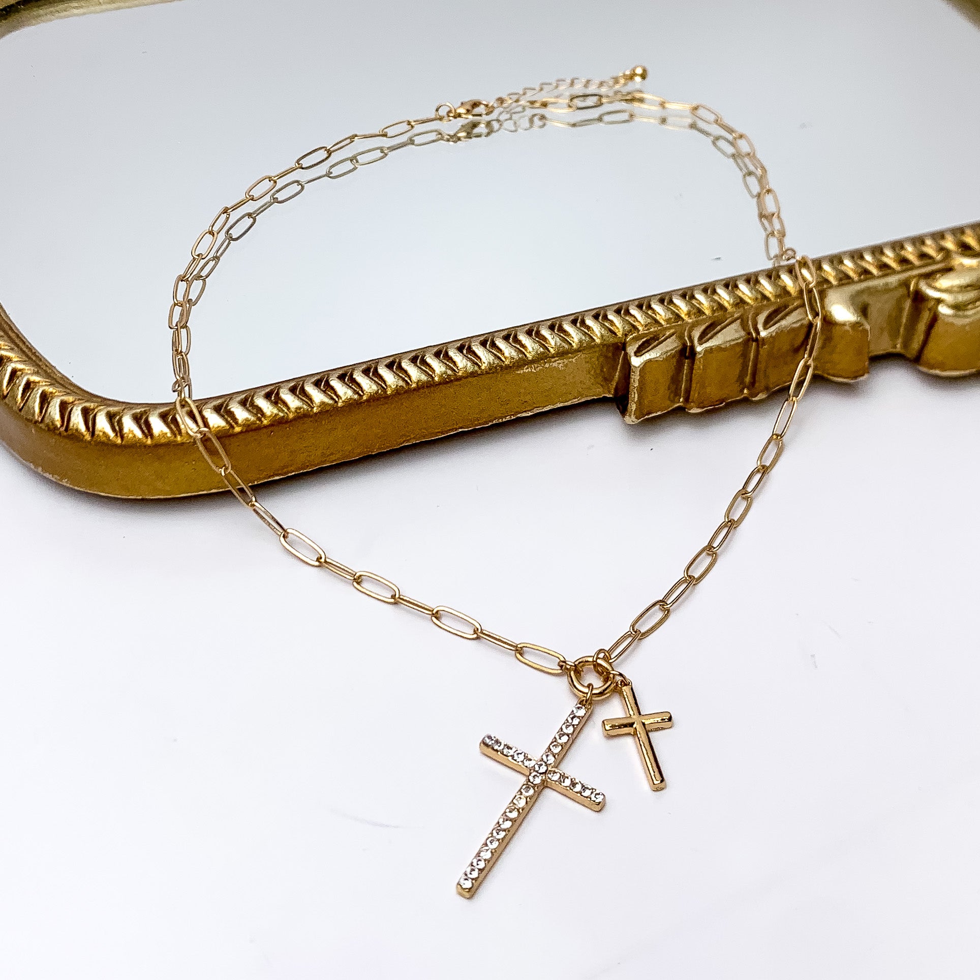 Gold Tone Double Cross Chain Necklace With Clear Crystals. Pictured on a white background with part of the necklace on a gold trimmed necklace.
