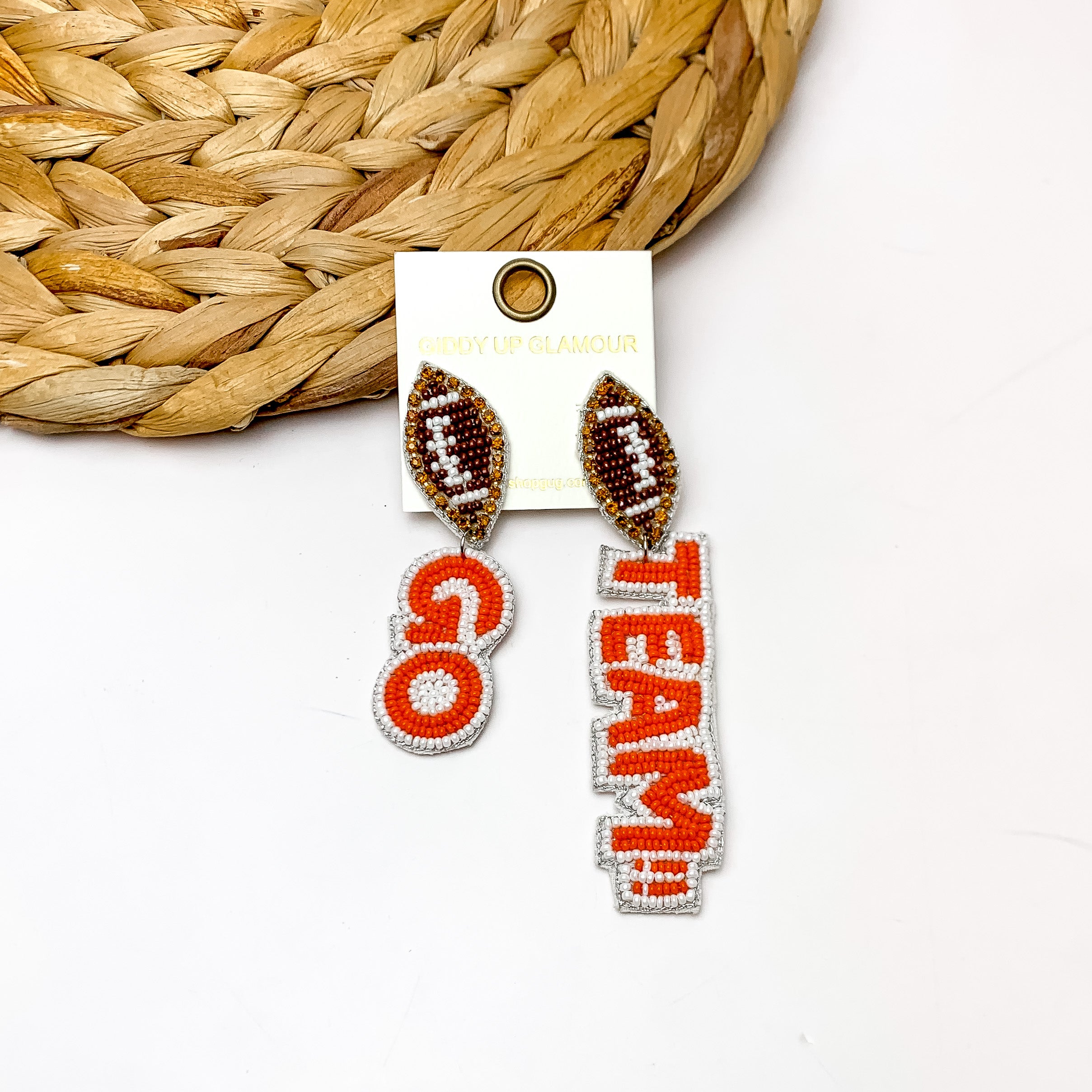 " Go Team!!" Beaded Earrings With Football Posts in Orange and White. These earrings are laying against a woven piece with a white background behind it.