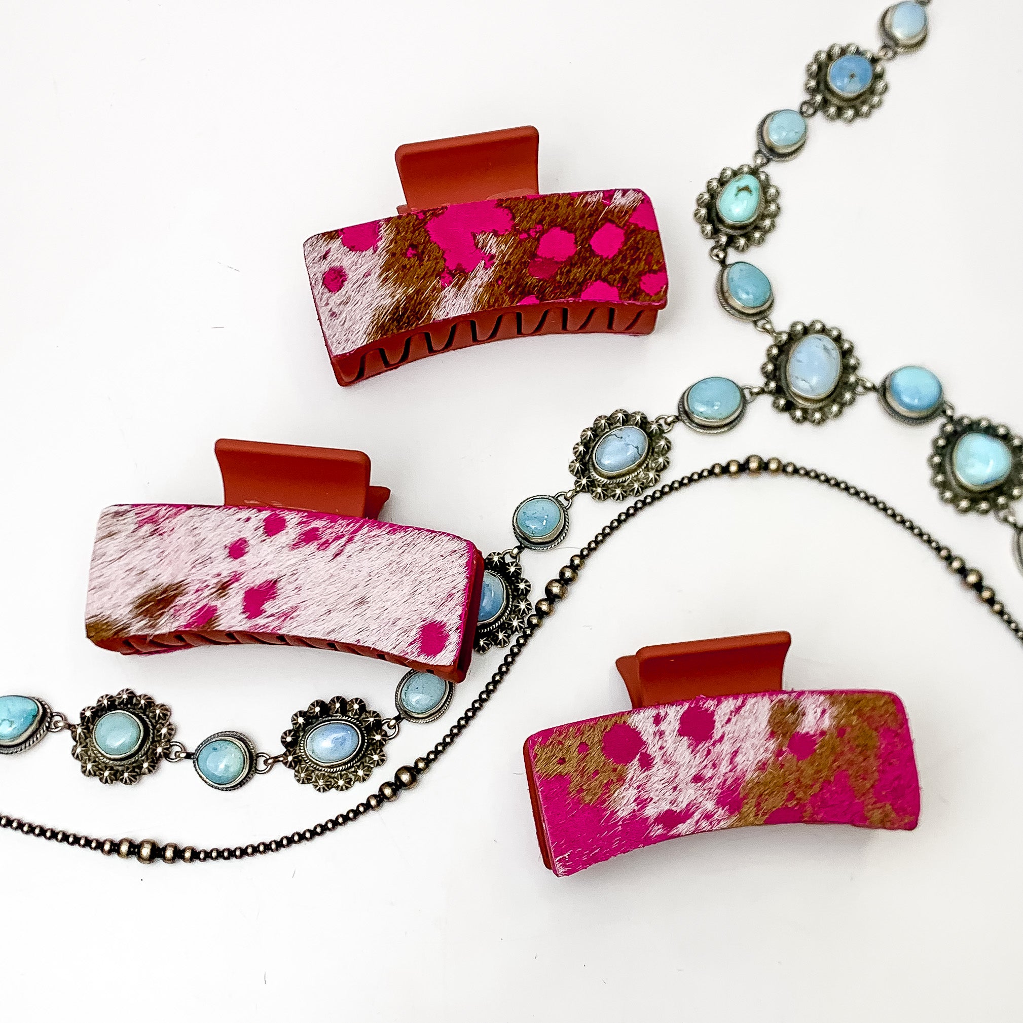 Pictured are three rust red hair clips with pink mix hide patches. These earrings are pictured on a white background with silver necklaces under the clips. 
