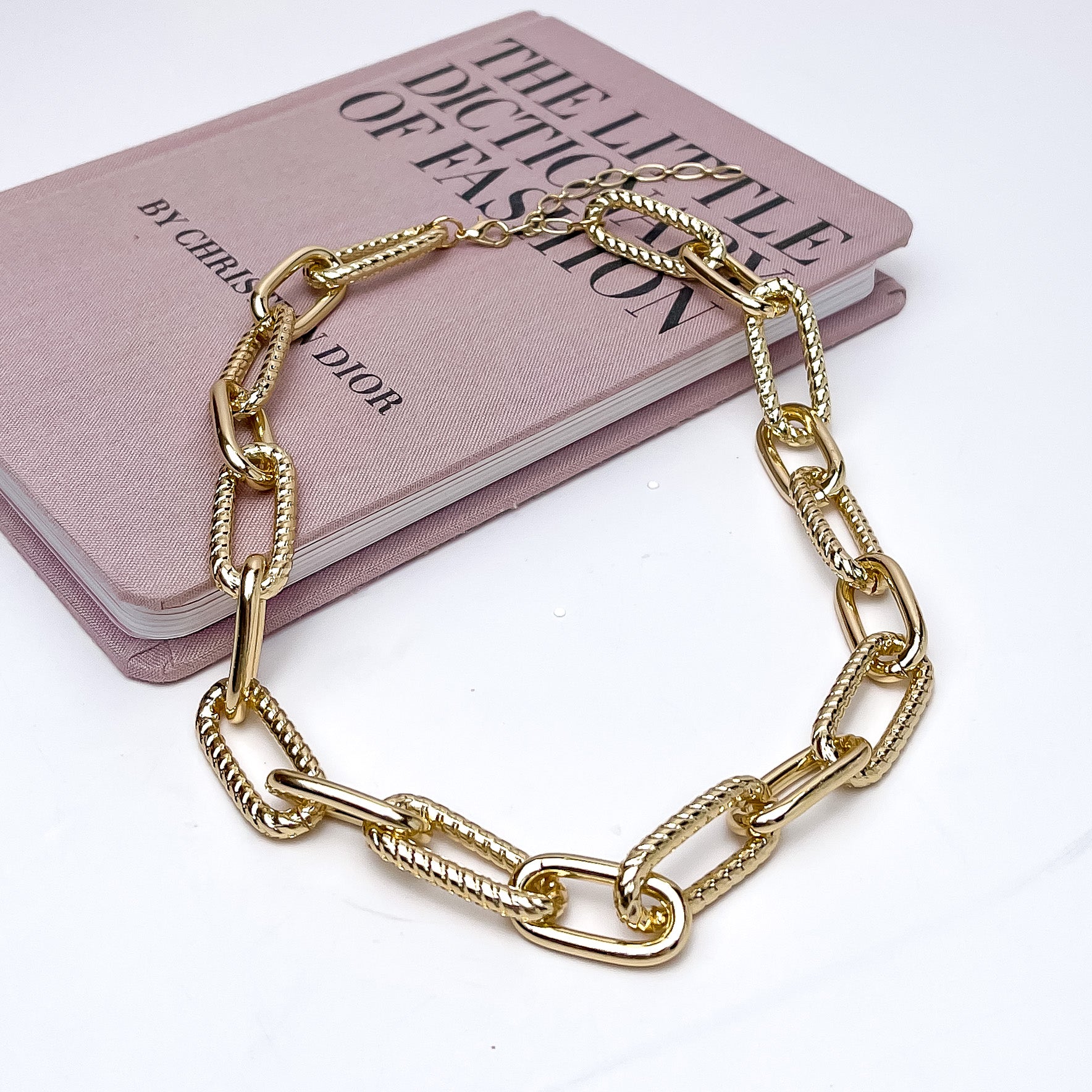 The Weekender Gold Tone Chain Necklace. This necklace is pictured on a white background with part of it on a pink book.