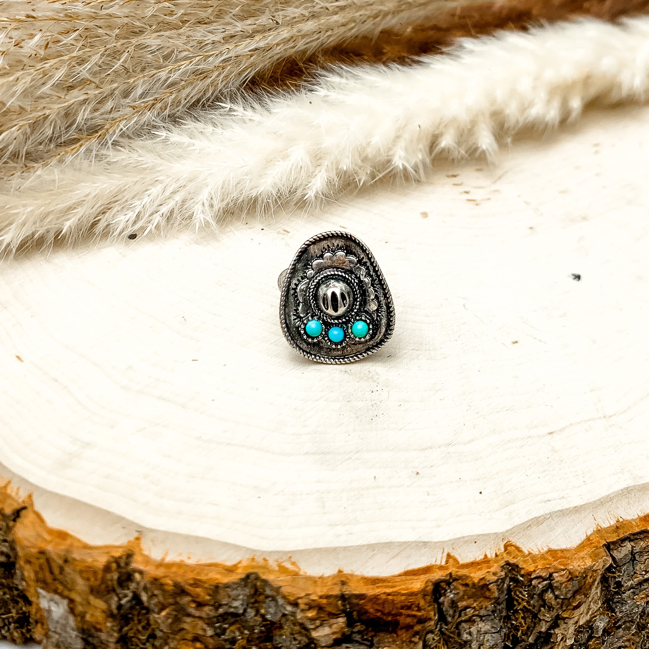 Cowgirl Silver Tone Ring With Turquoise Blue Stones. Silver cowboy hat ring sitting on a wood piece with feathers in the back.