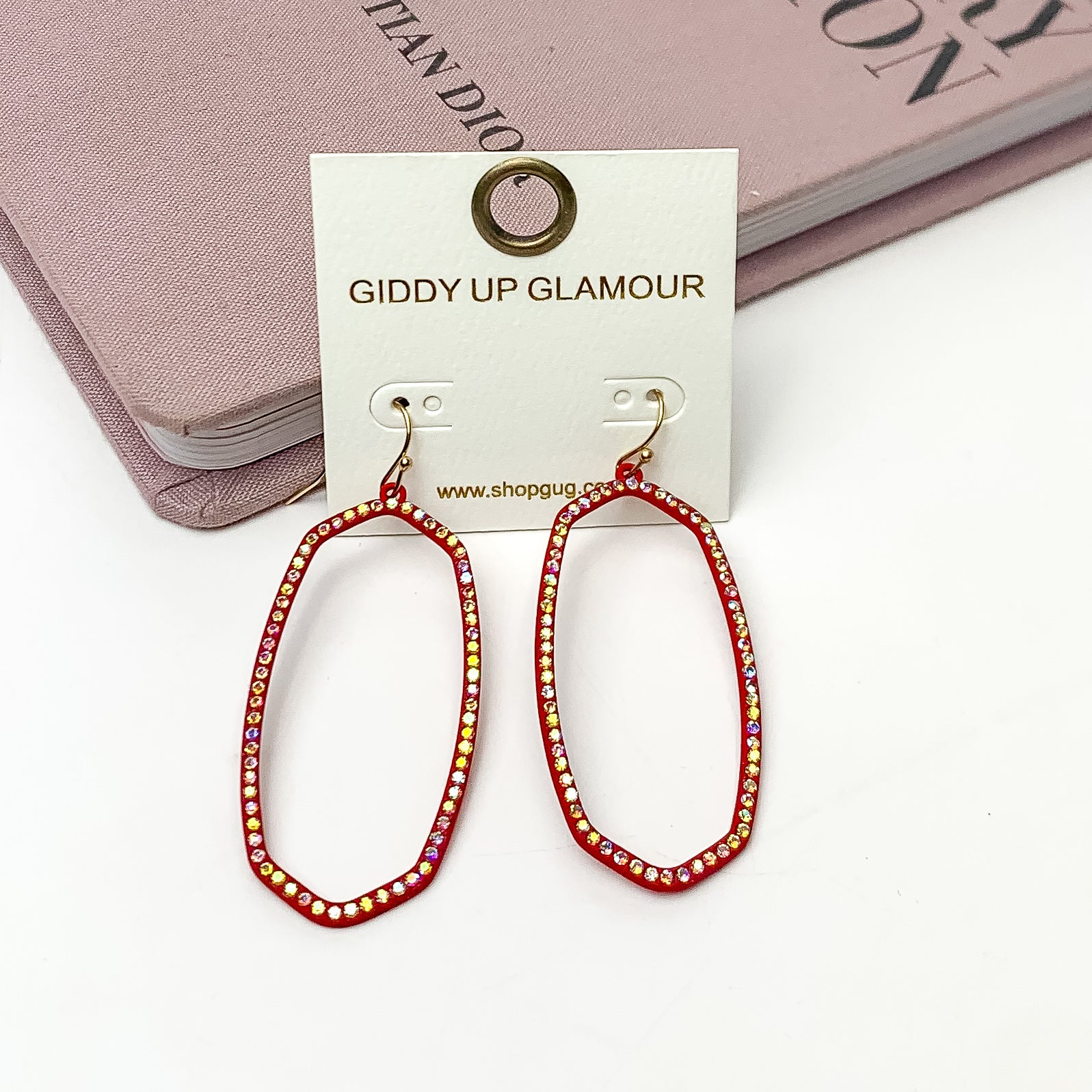 Sparkle Girl Open Oval Earrings in Hot Pink. These earrings are pictured laying against a pink book with a white background.