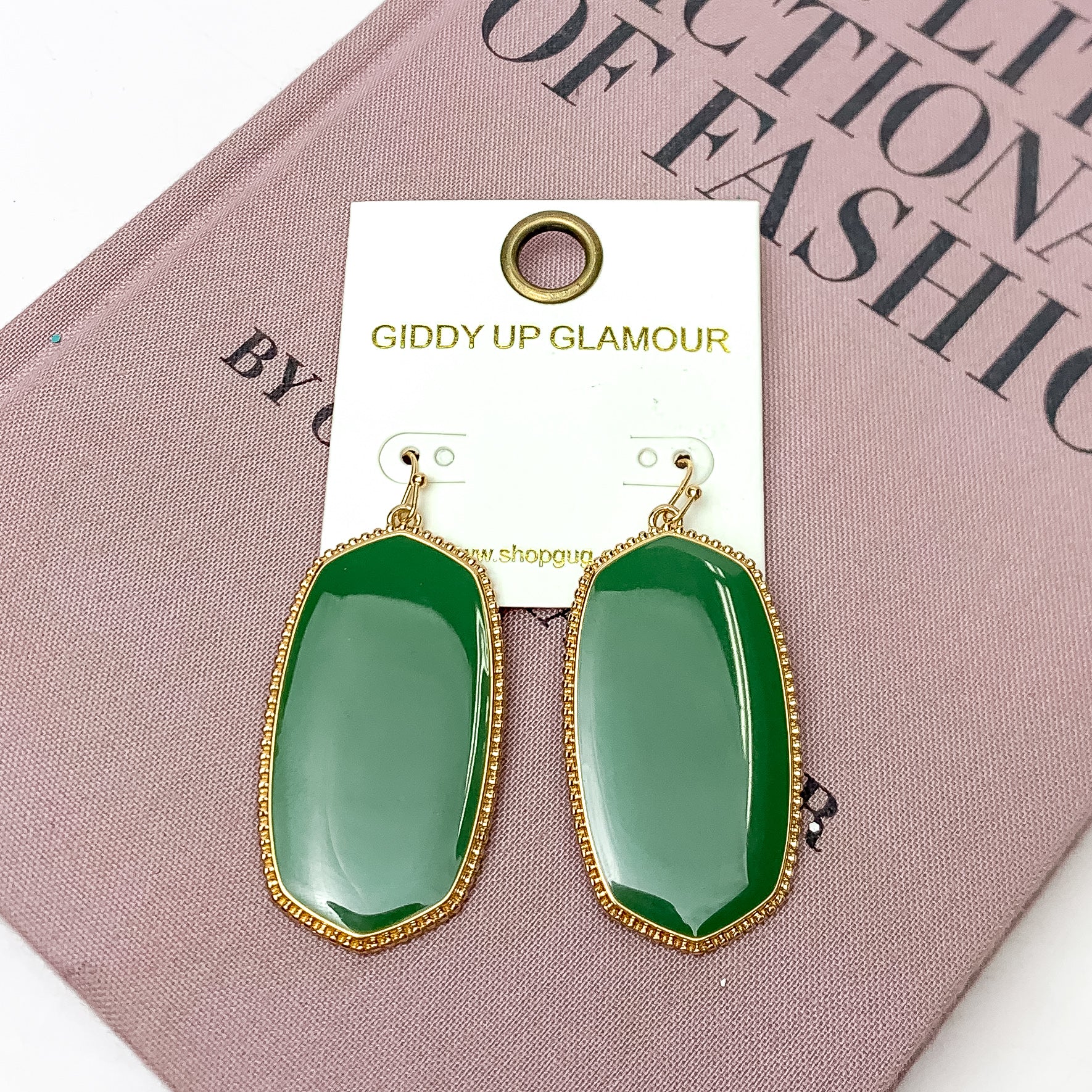 Southern Charm Oval Earrings in Olive Green. These earrings are laying on a pink book with a white background behind the book.