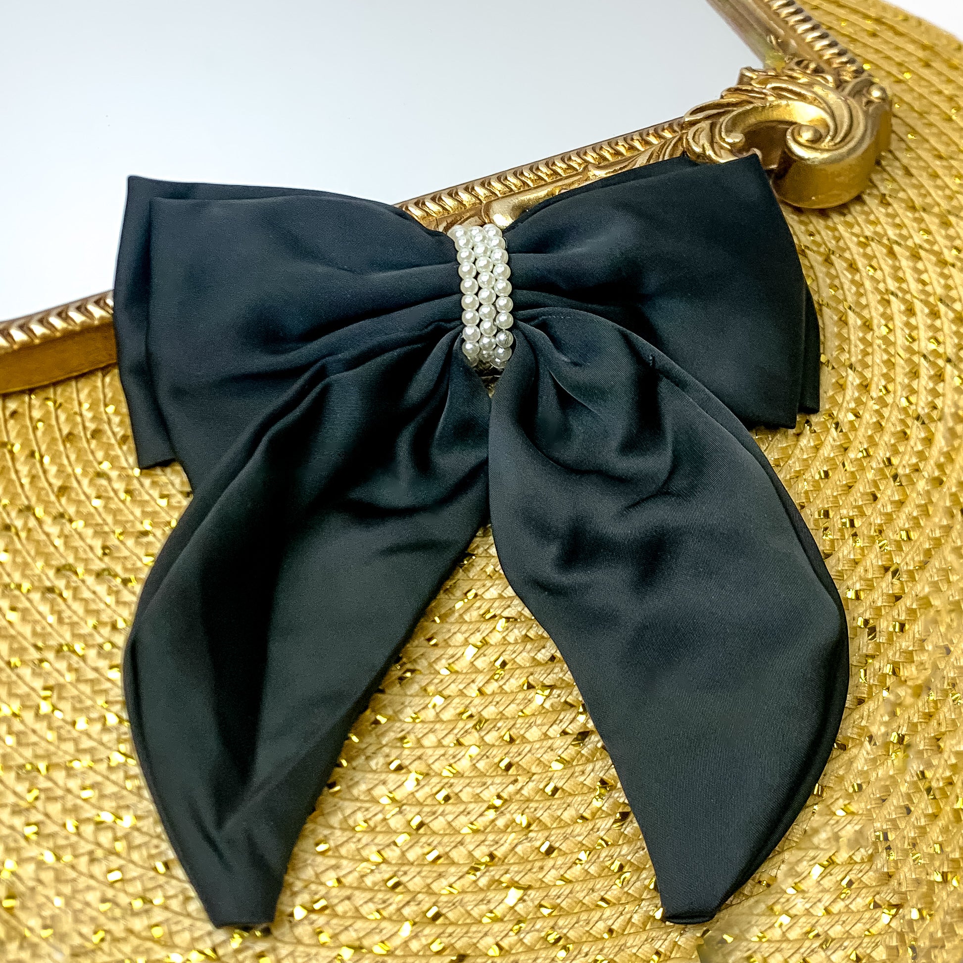 This layered black bow with a pearl canter is laid against a gold mirror and has a gold background.