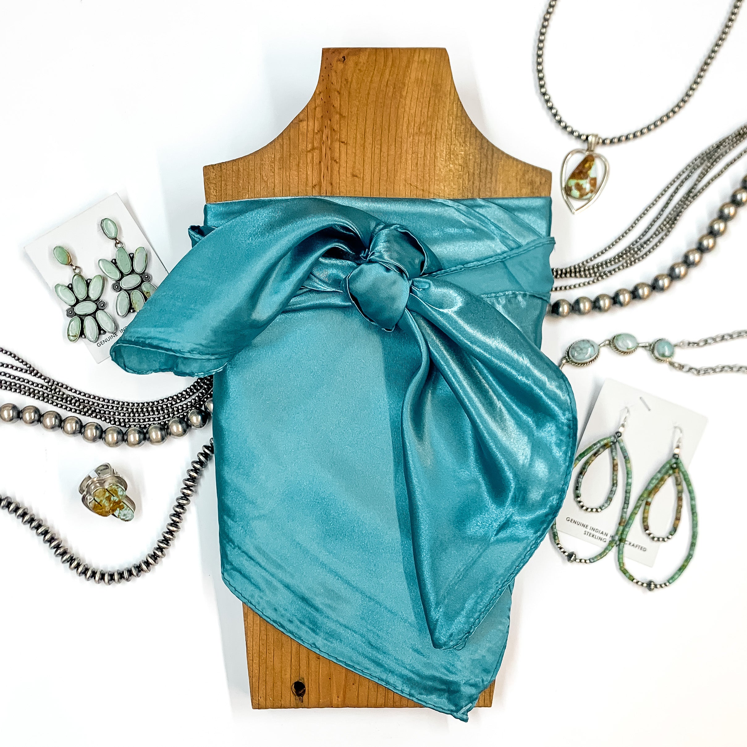 Solid colored scarf in Tuff turquoise. Scarf is tied around a wooden piece. The scarf and piece of wood is pictured on a white background with Navajo jewelry spread out around it.