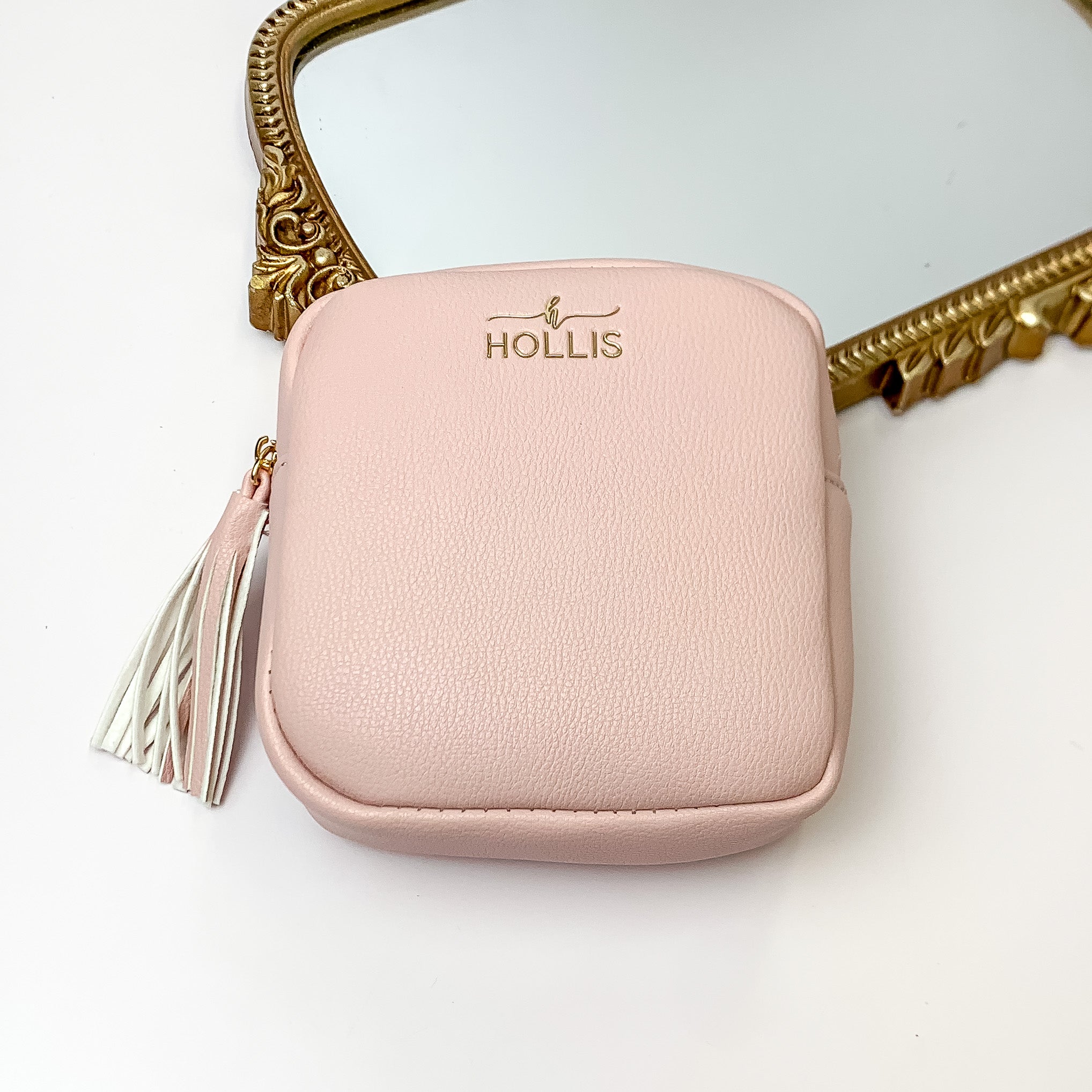 Blush pink square pouch that is pictured in front of a gold mirror on a white background. 
