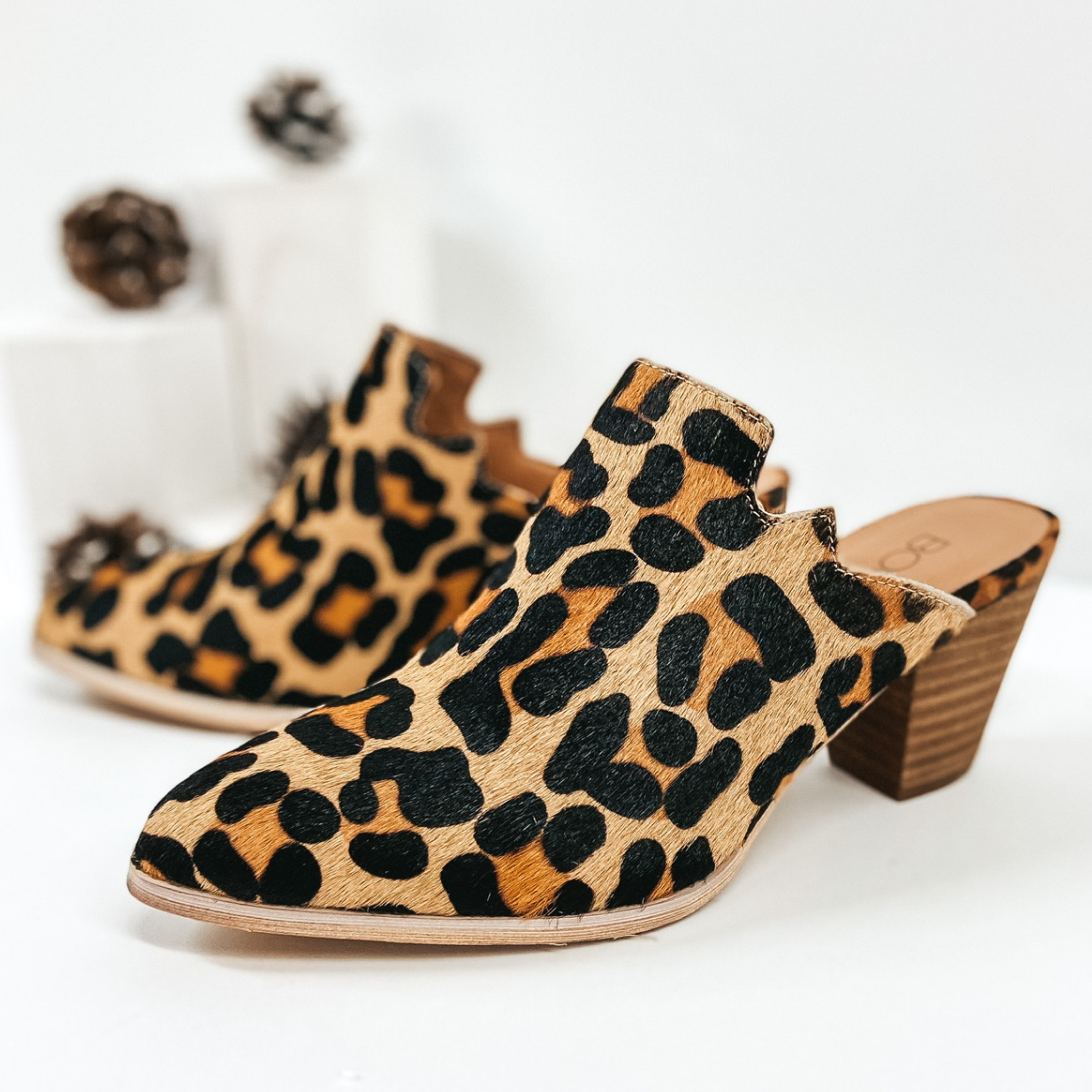 Leopard print hair on hide heeled mules. Pictured on white background with pinecones.