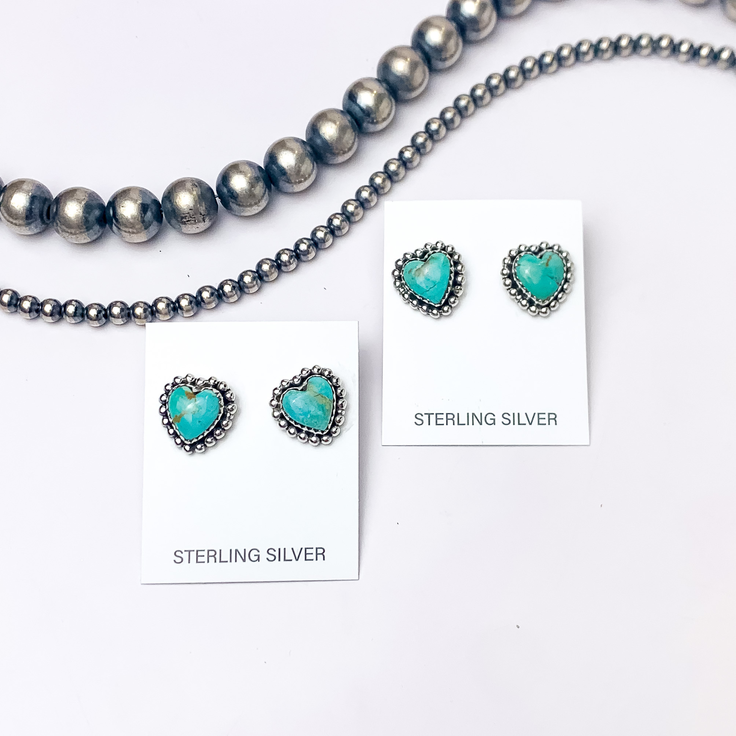 In the picture are handmade sterling silver heart shaped stud earrings with kingman turquoise remix stones with a white background