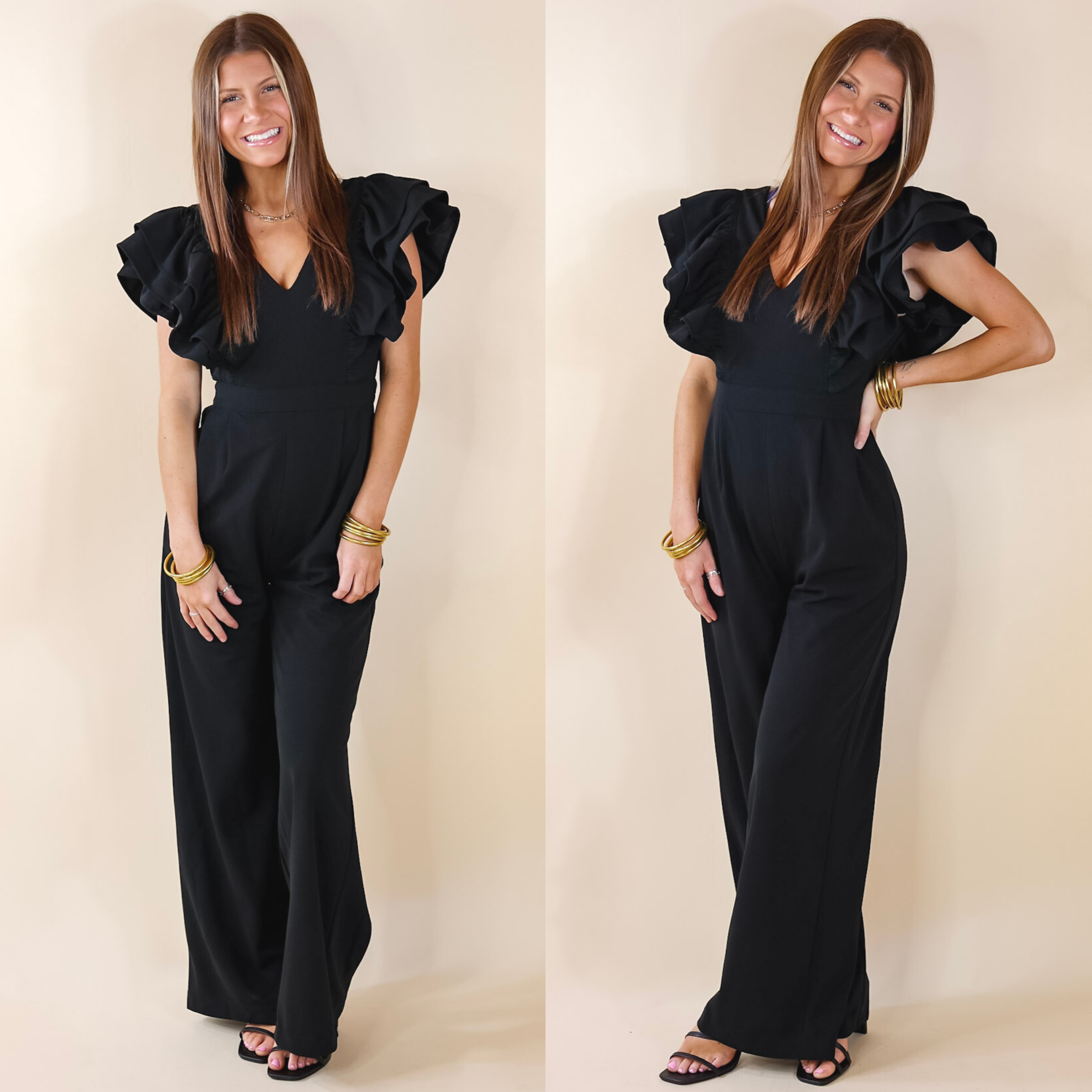 Model is wearing a black jumpsuit with ruffle sleeves and a v neckline. Model has it paired with black heels and gold jewelry.