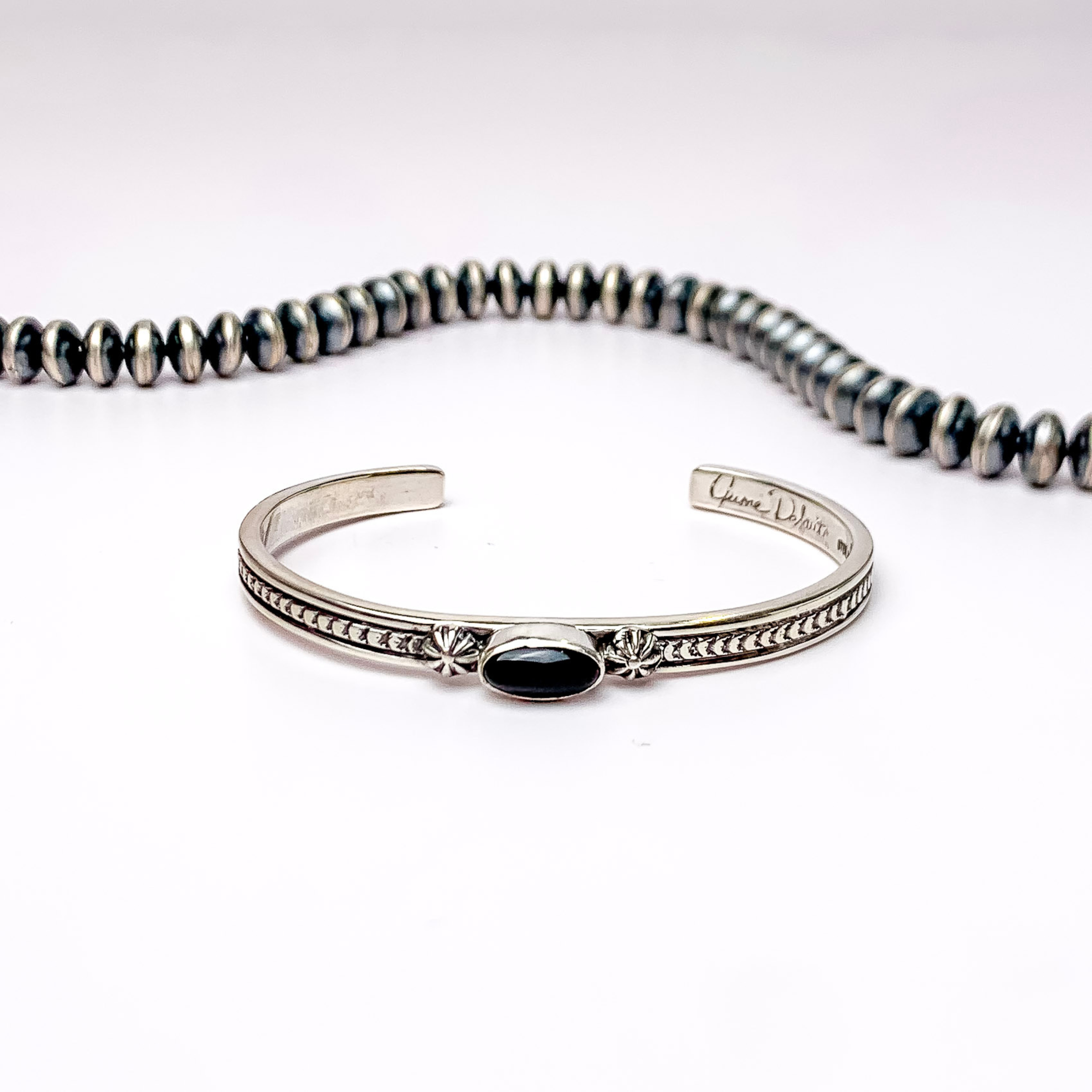 Centered in the picture is a sterling silver braclet with a black stone in the middle with a white background.