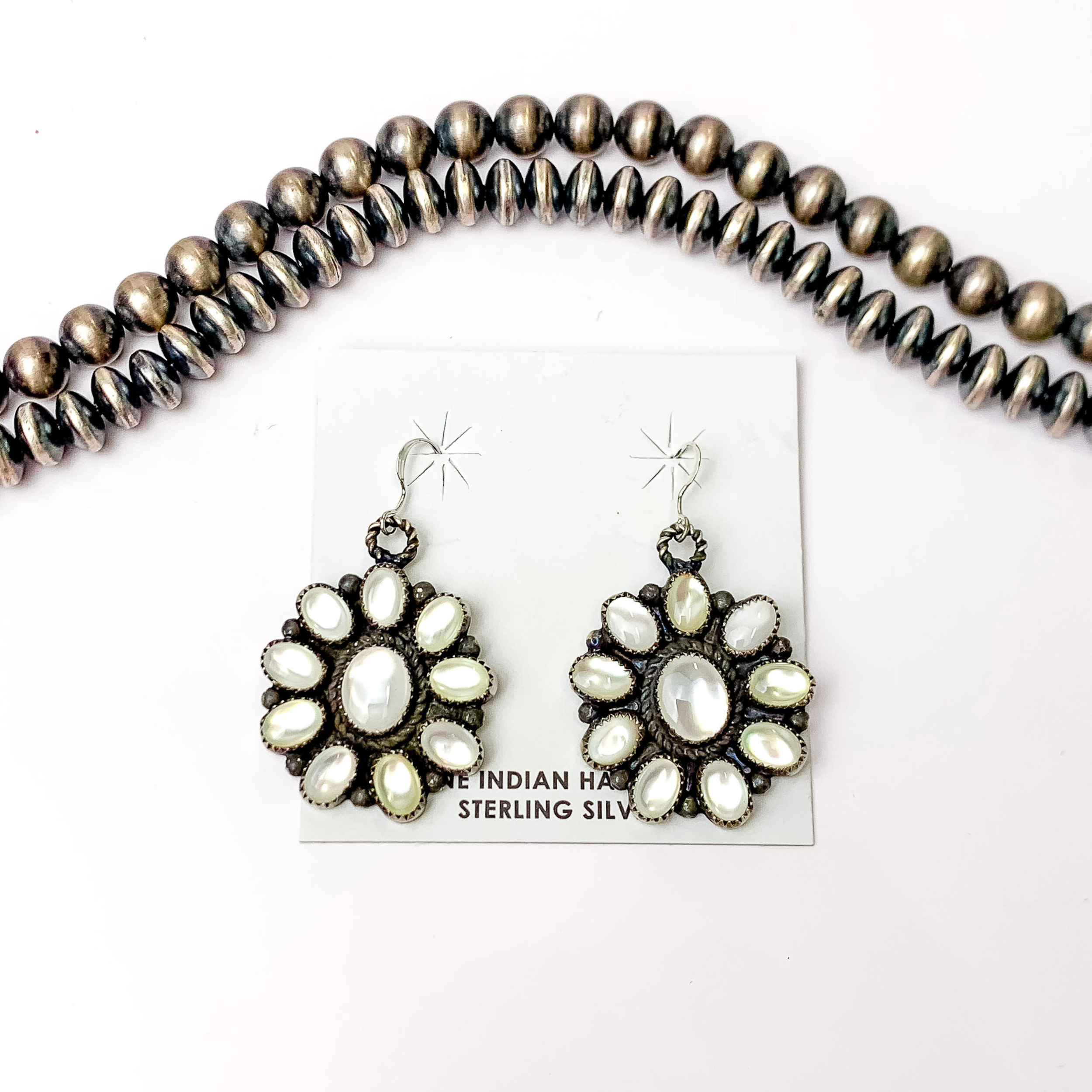 Centered in the picture are white pearl sterling silver dangling earrings with a white background. 