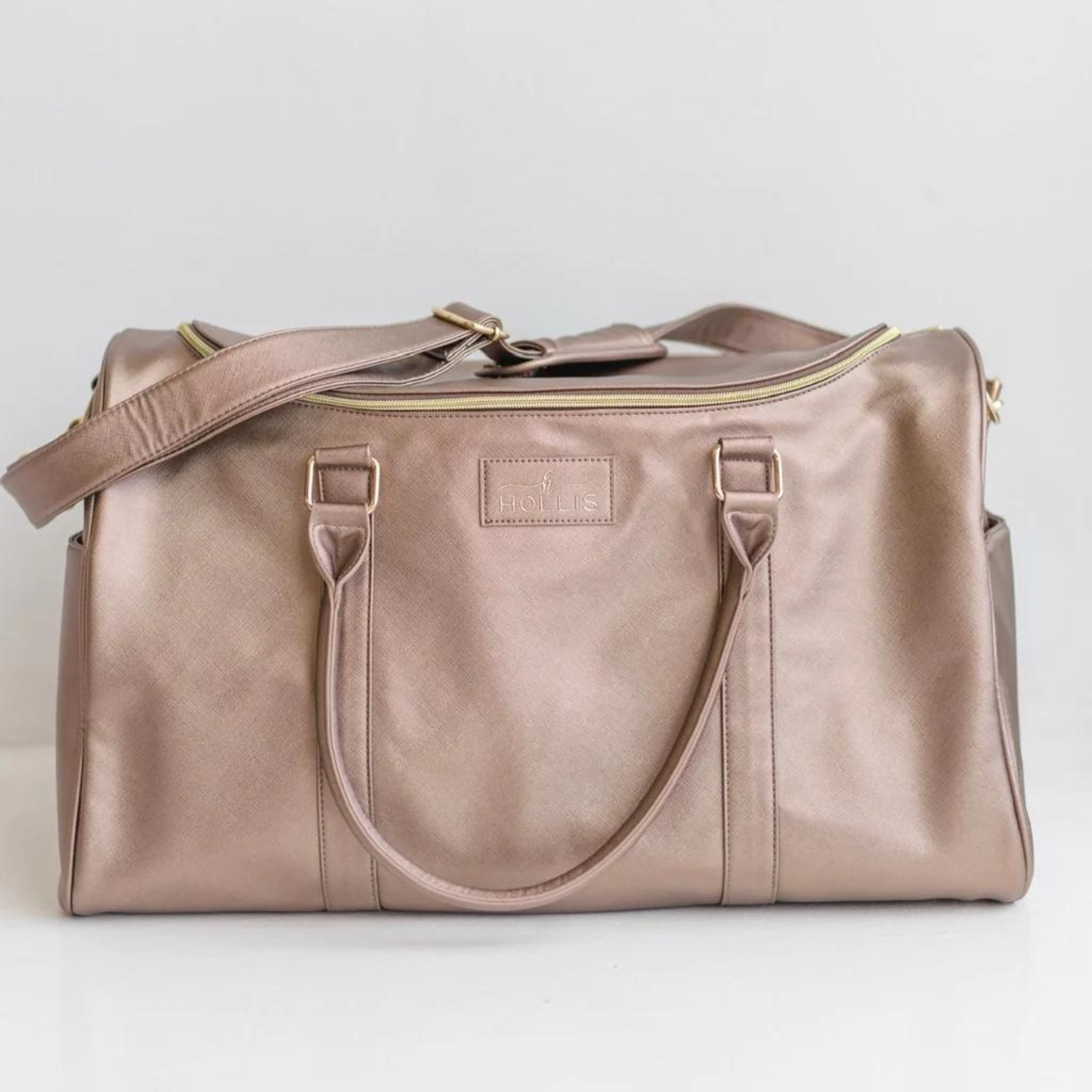 Metallic mocha duffel bag with hot pink handles. This bag has a gold top zipper and pocket on each side. This bag is pictured on a light grey background. 