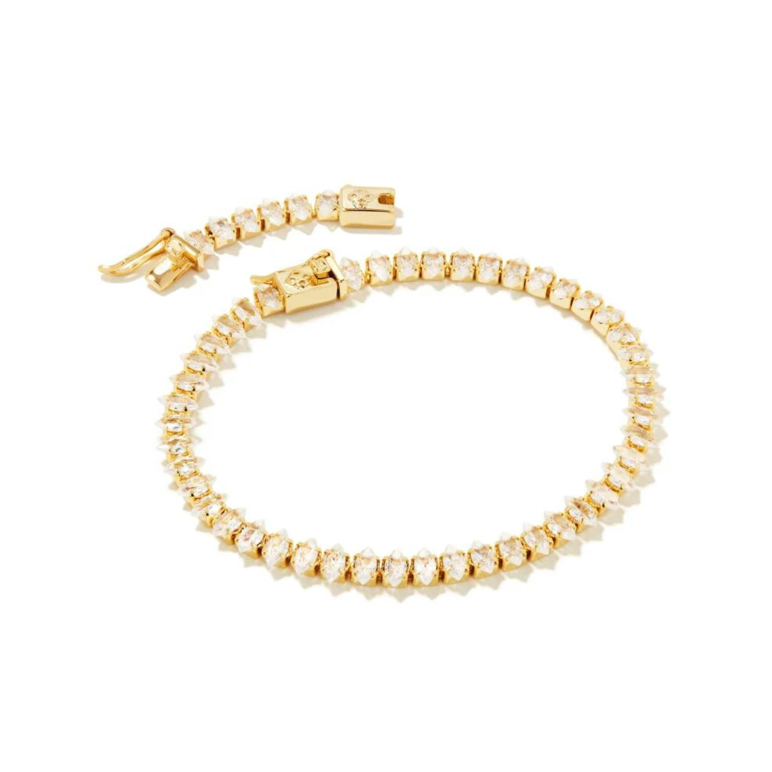 Pictured is a clear crystal tennis bracelet in gold on a white background.
