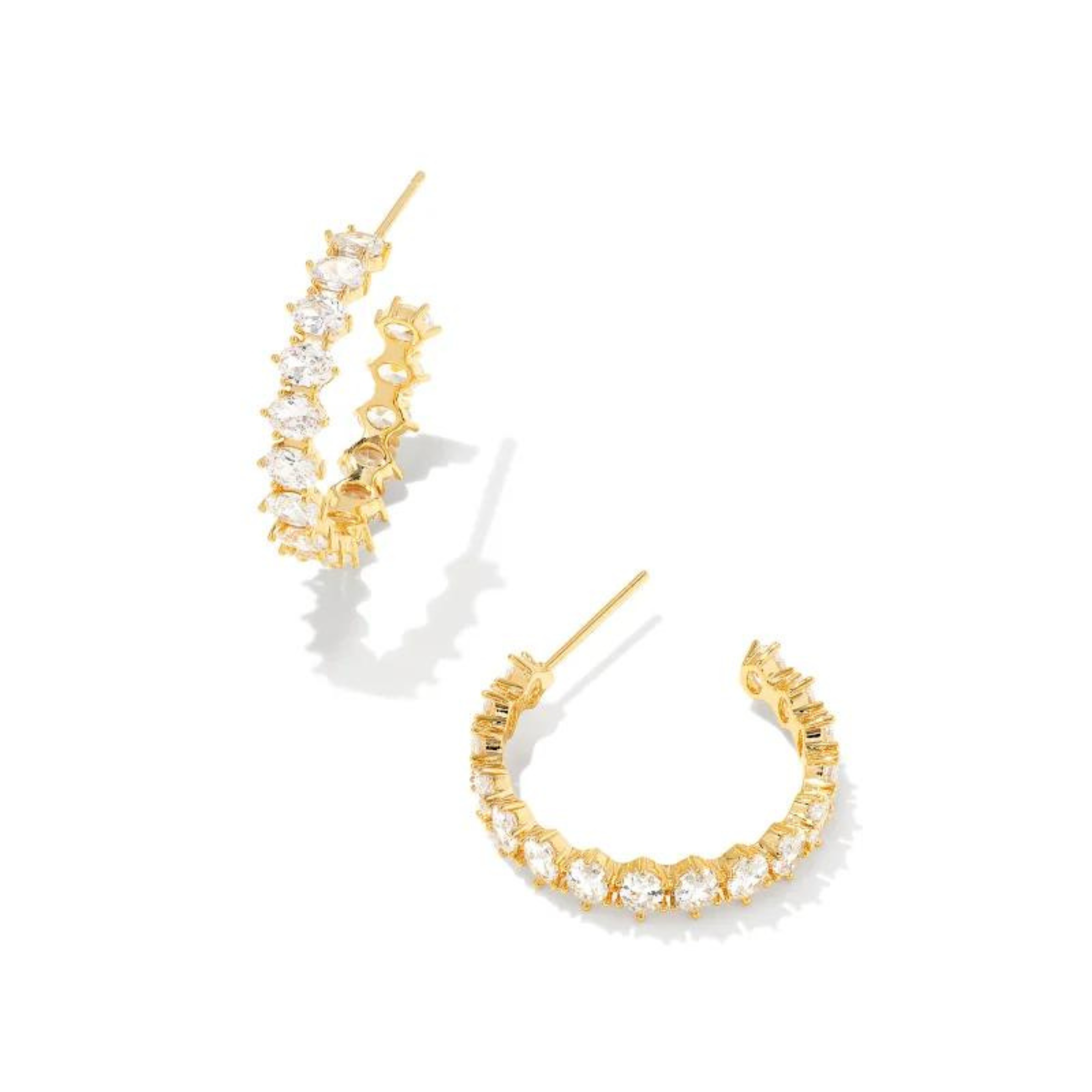 Pictured on a white background is a pair of gold hoop earrings with a oval, clear crystals. 