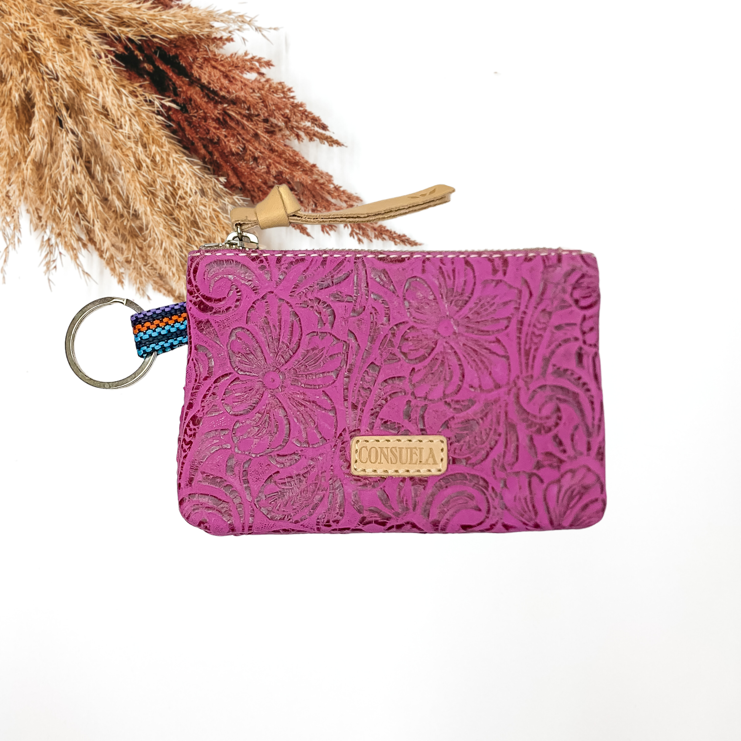 Pictured on a white background is a fuchsia, leather tooled pouch with a silver key ring and a leather tassel on the zipper. 