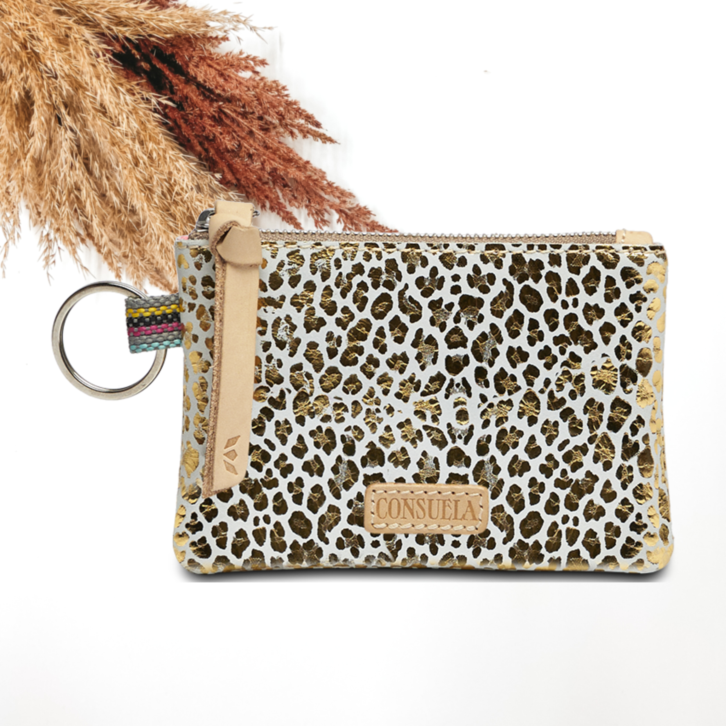 Pictured on a white background is a pouch with a light tan leather zipper pull on the yop and a silver key ring on the side. This pouch has a white with a metallic gold leopard print design. 