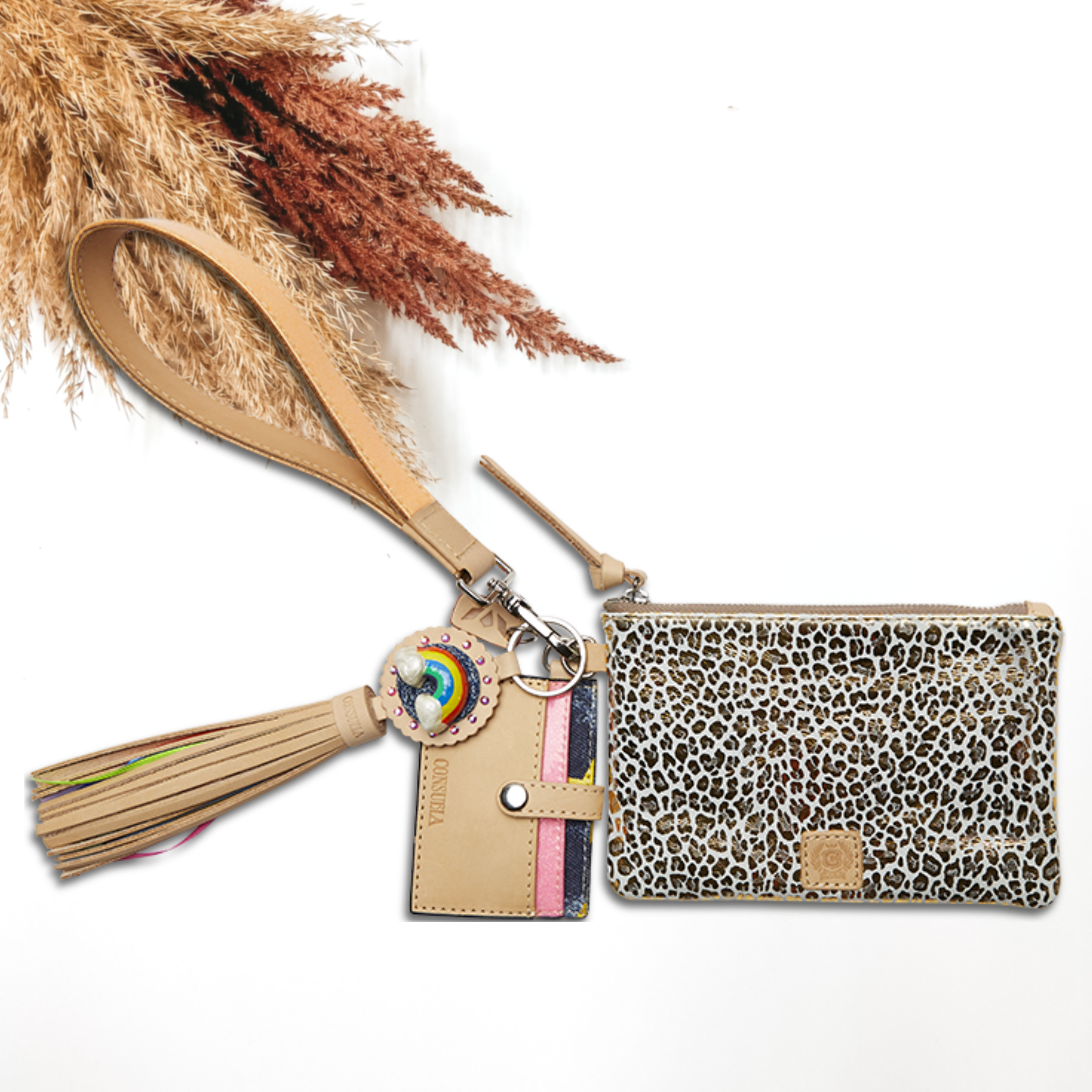 Pictured on a white background is a white and gold leopard print pouch with a light tan and light orange glitter wristlet. This pouch also includes a rainbow charm, light tan tassel on the zipper, and a card holder keychain.