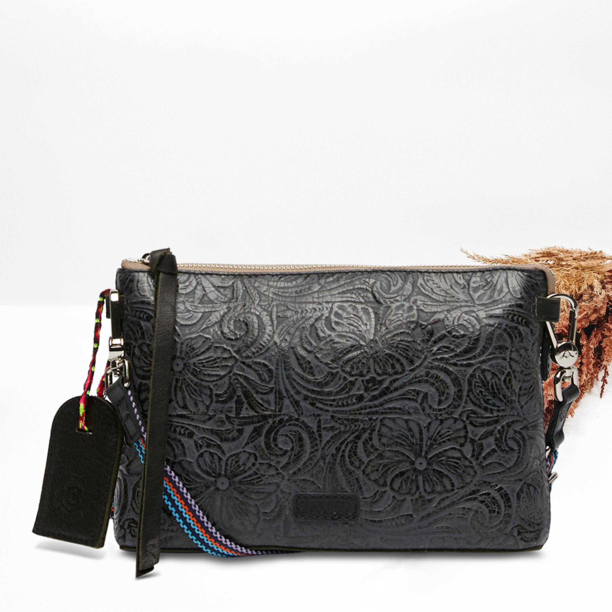 Pictured on a white background is an midtown corssbody purse with a black leather wristlet strap and a woven crossbody strap. This purse has a white with a black leather tooled print.