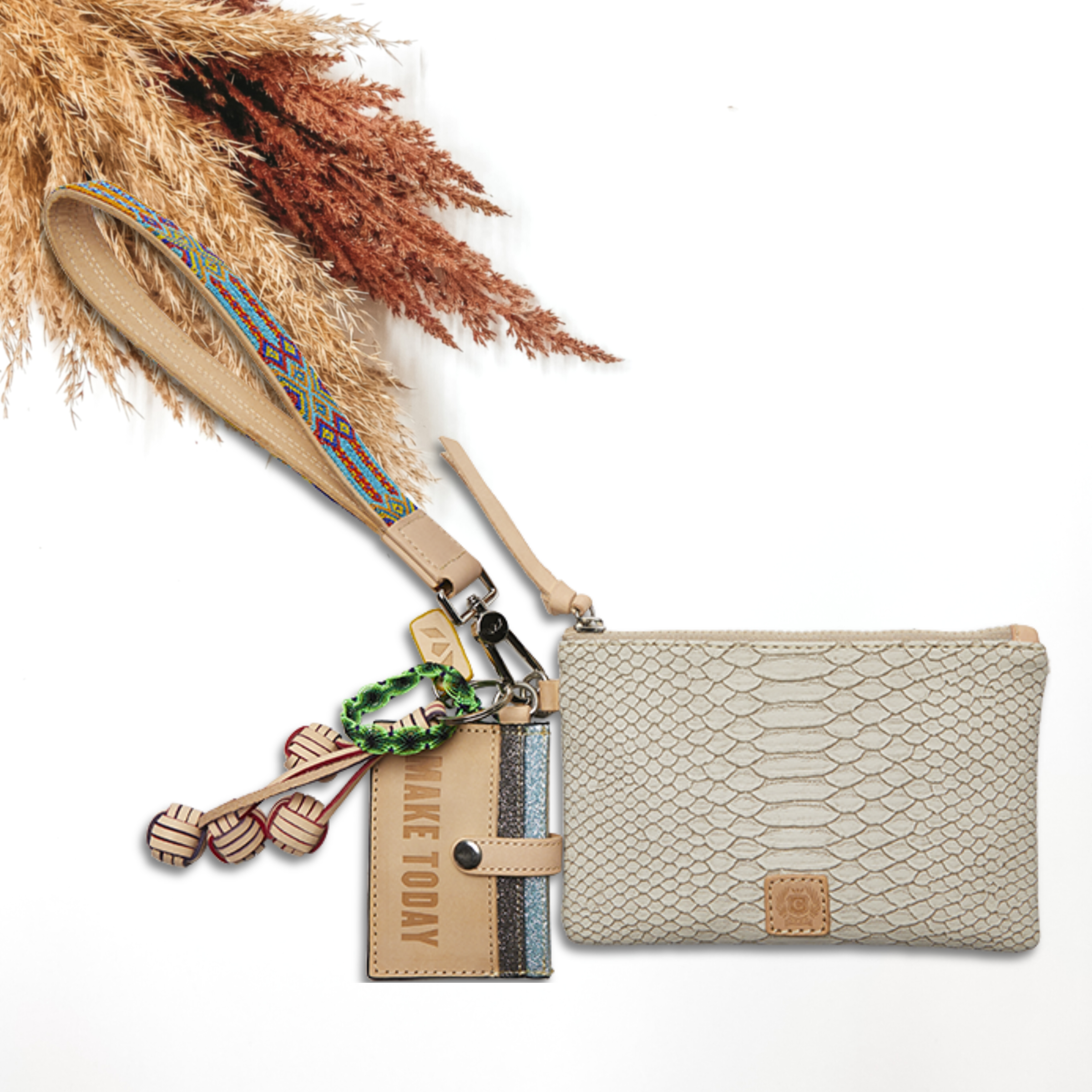 Pictured on a white background is a snake print pouch with a multicolor embroidered wristlet. This pouch also includes a tan charms, light tan tassel on the zipper, and a card holder keychain.