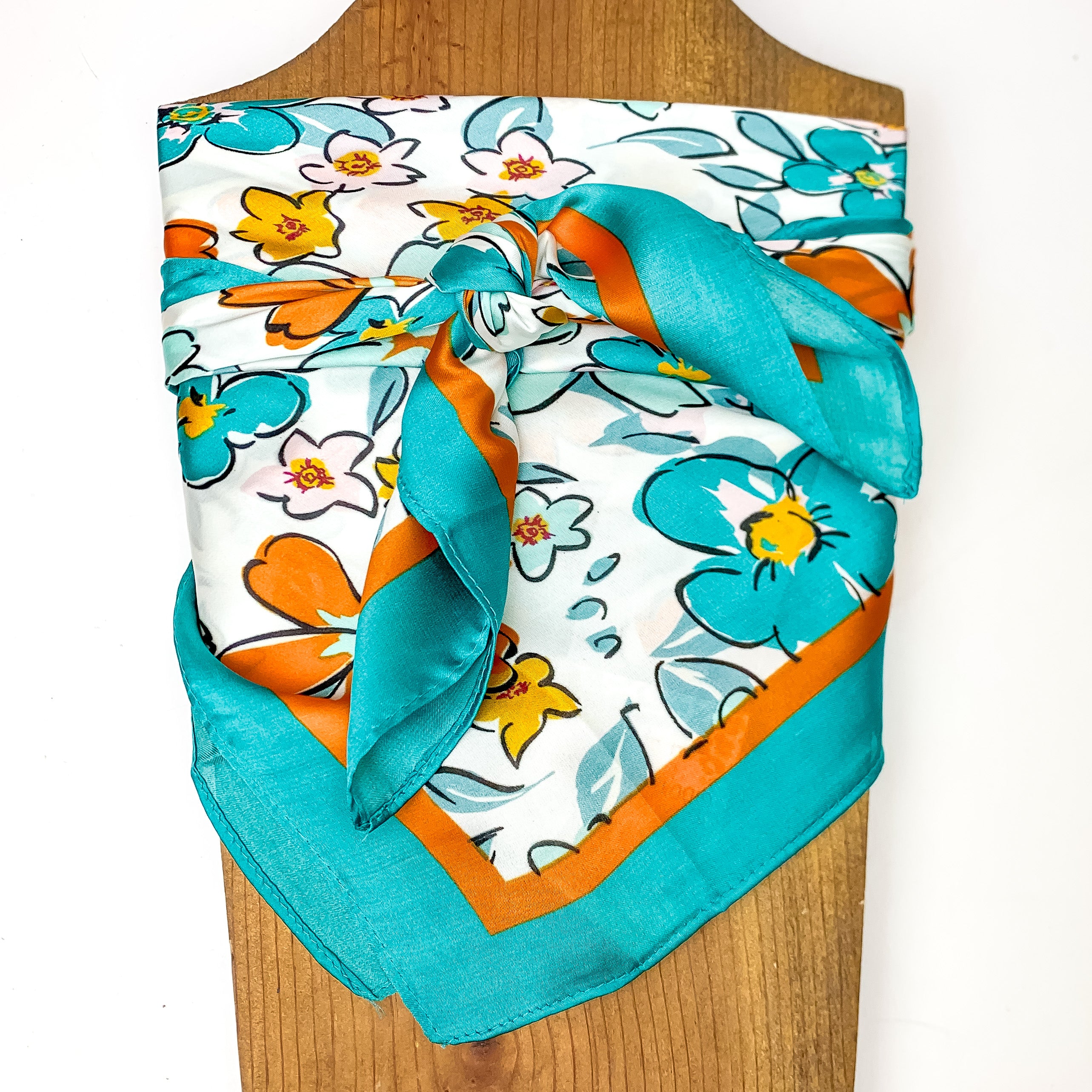 Flower Print Wild Rag in Teal Blue. This scarf is pictured tied around a wood piece with a white background.
