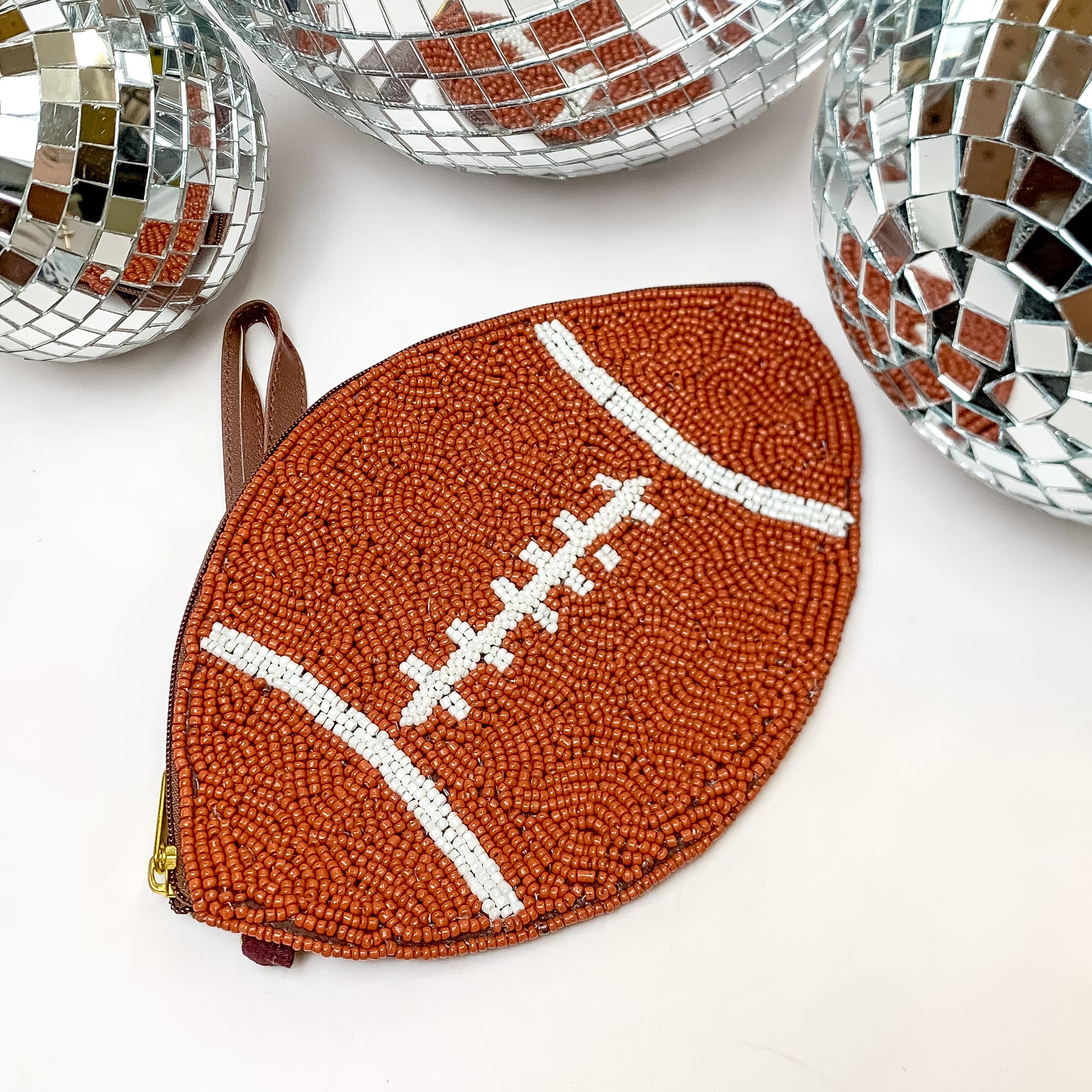 Beaded brown football wristlet. This wristlet is laying on a white background with disco balls around it for decoration.