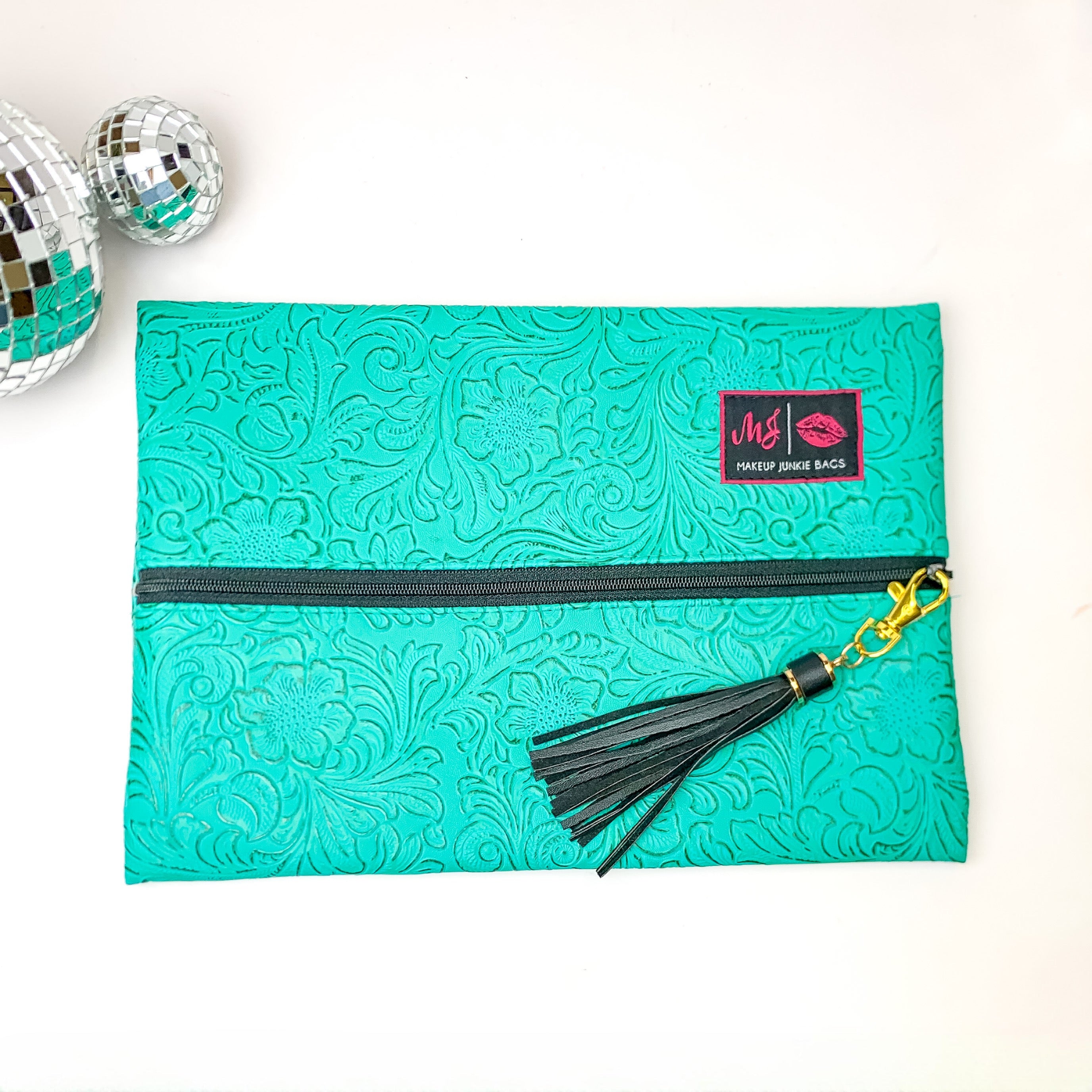 Pictured on a white background with disco balls at top is a lay flat bag in a turquoise leather tooled print. This bag includes a middle zipper and a tassel.